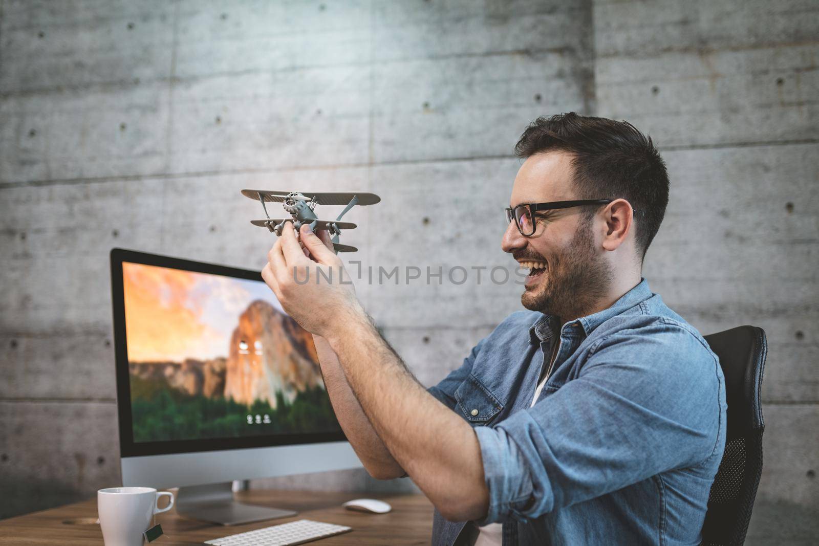 Young handsome successful smiling freelance entrepreneur having fun and showing little model of airplane, explaining how it flies.