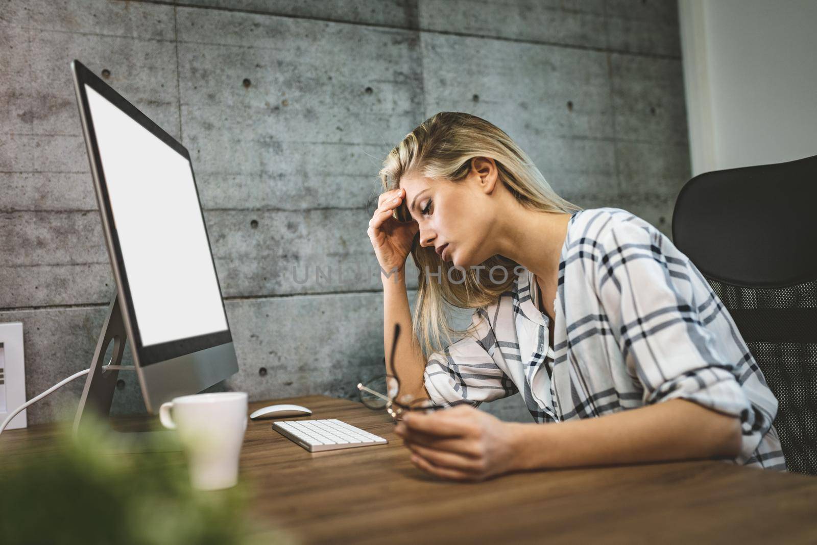 Young handsome frustrated and stressed business woman sitting at the office front a computer and holding head.