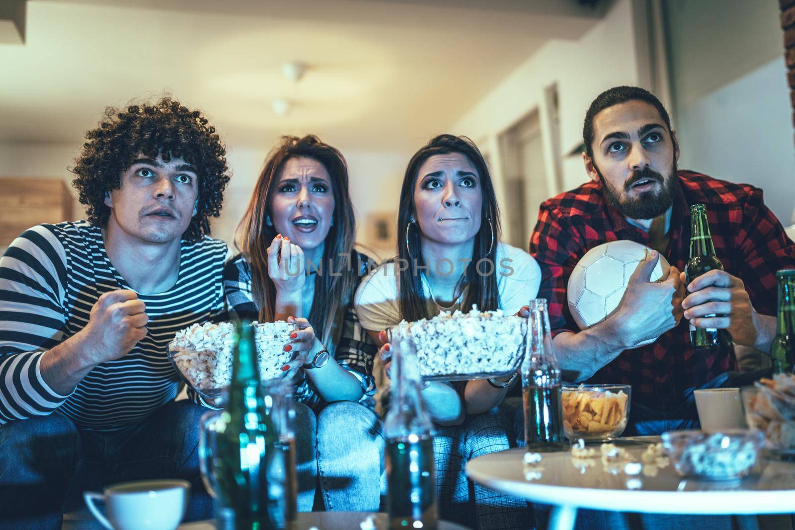 Friends are fans of sports games as football love spending their free time at home together. They are screaming and gesturing for a victory. 