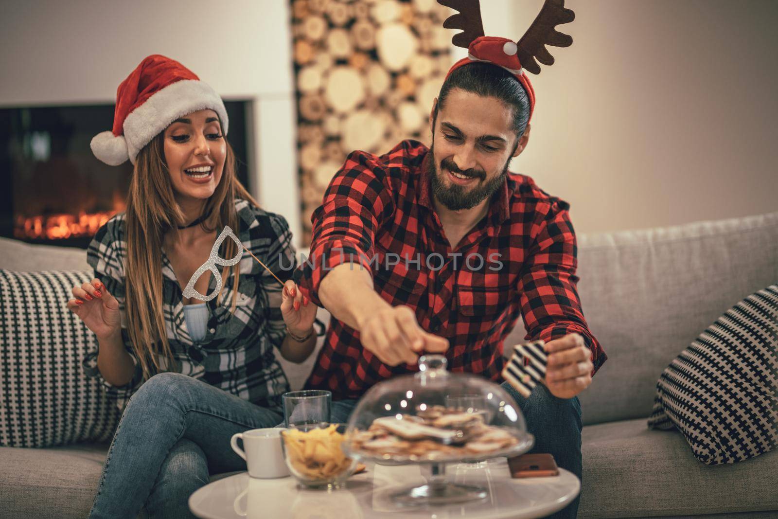 Cute beautiful couple is spending New Year eve at home sitting on sofa and eating cookies. They have great holidays having fun in nice company indoors.