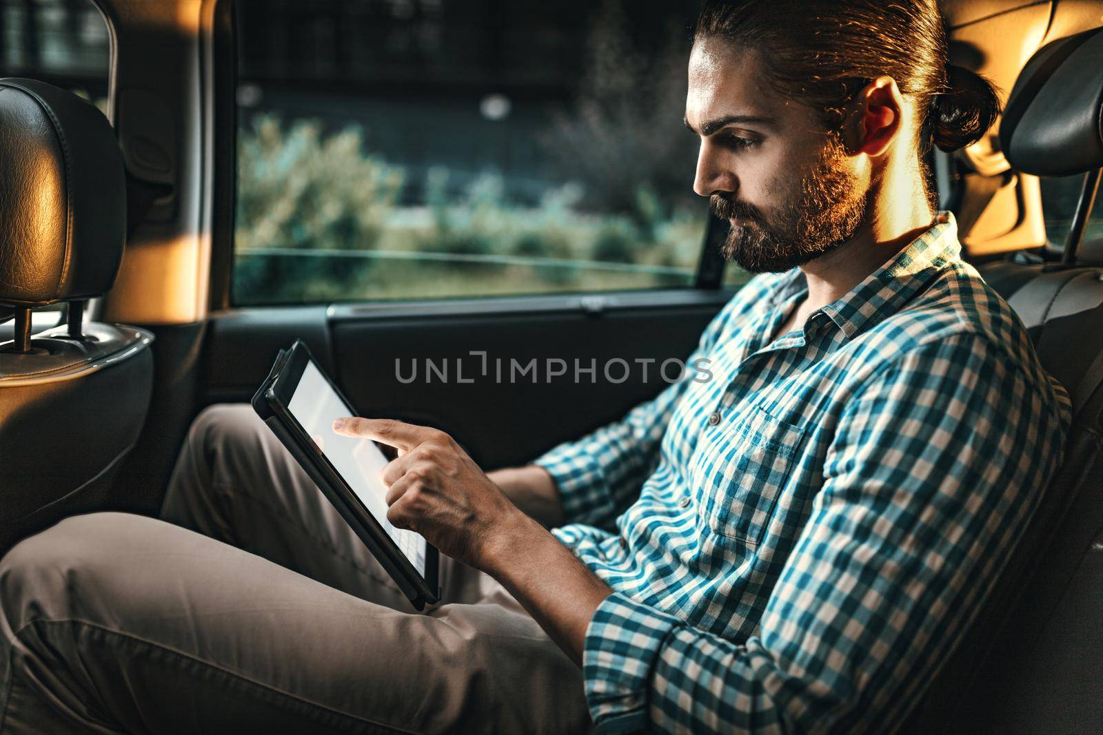 Young confident businessman is working on a business trip on the back seat in car.