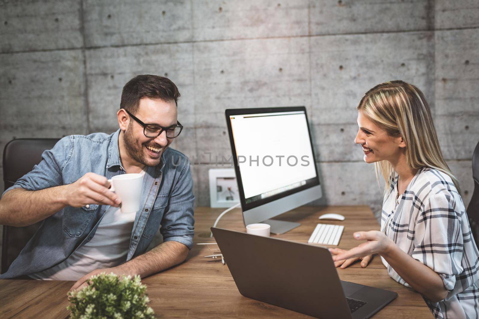 Young successful smiling colleagues talking about project which is leading to the top, in the office.