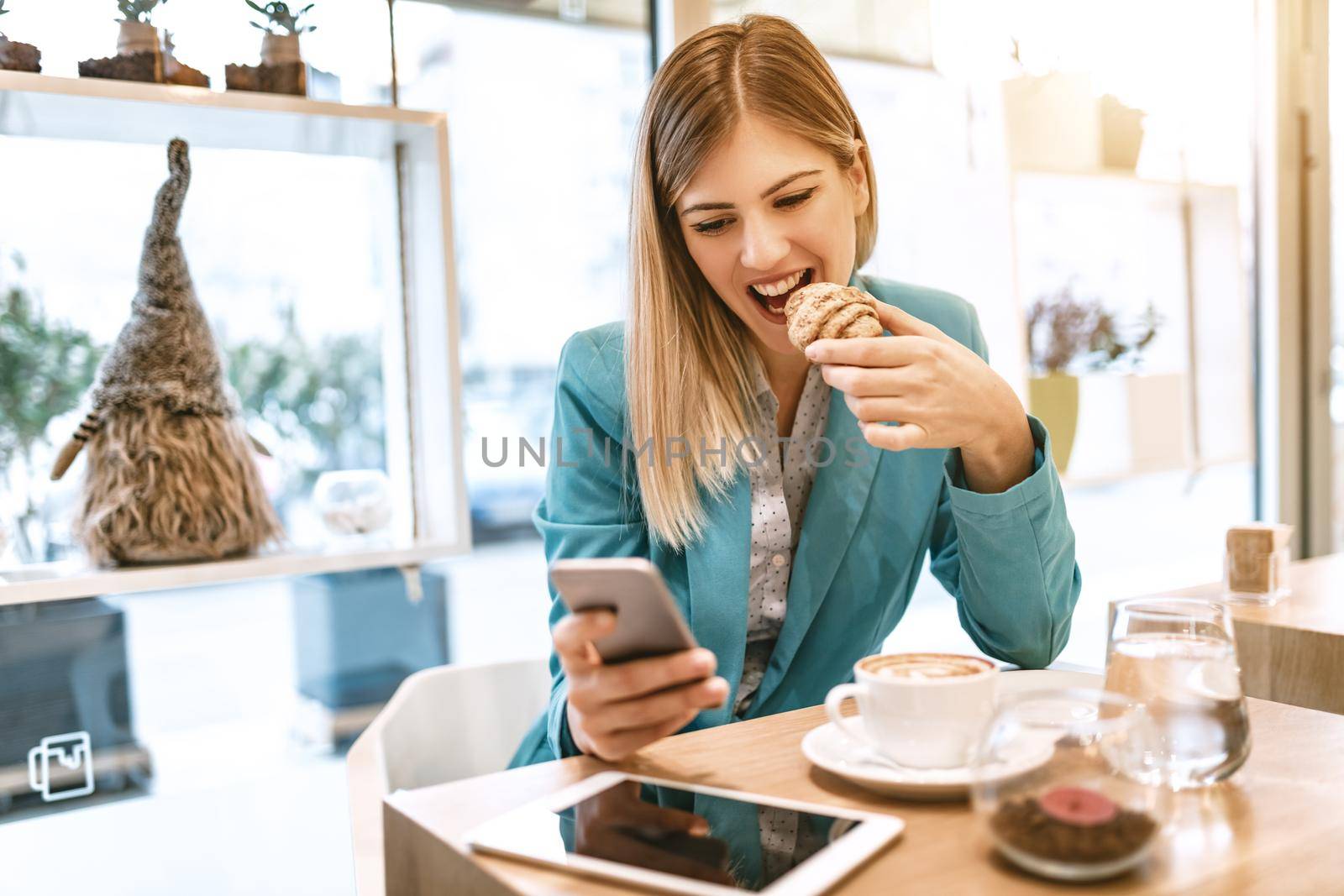 Young smiling businesswoman on a break in a cafe. He is having breakfast and using smartphone. 