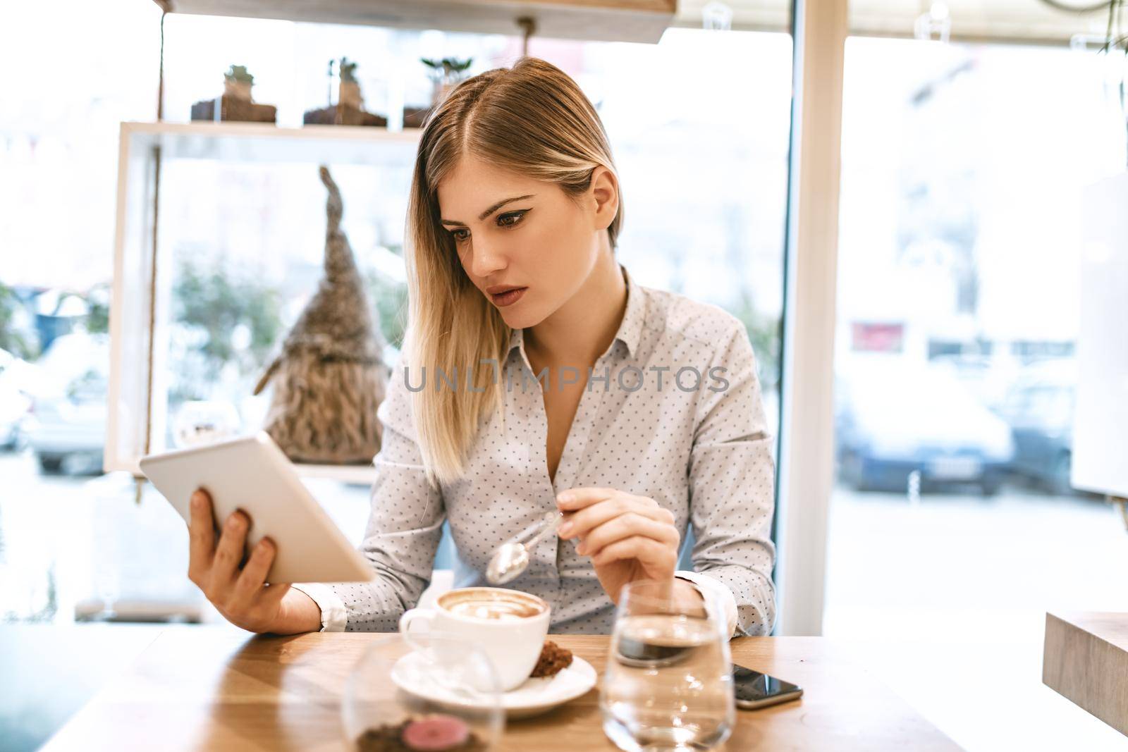 Beautiful young smiling woman drinking coffee in a cafe. She is surfing the internet on a digital tablet.