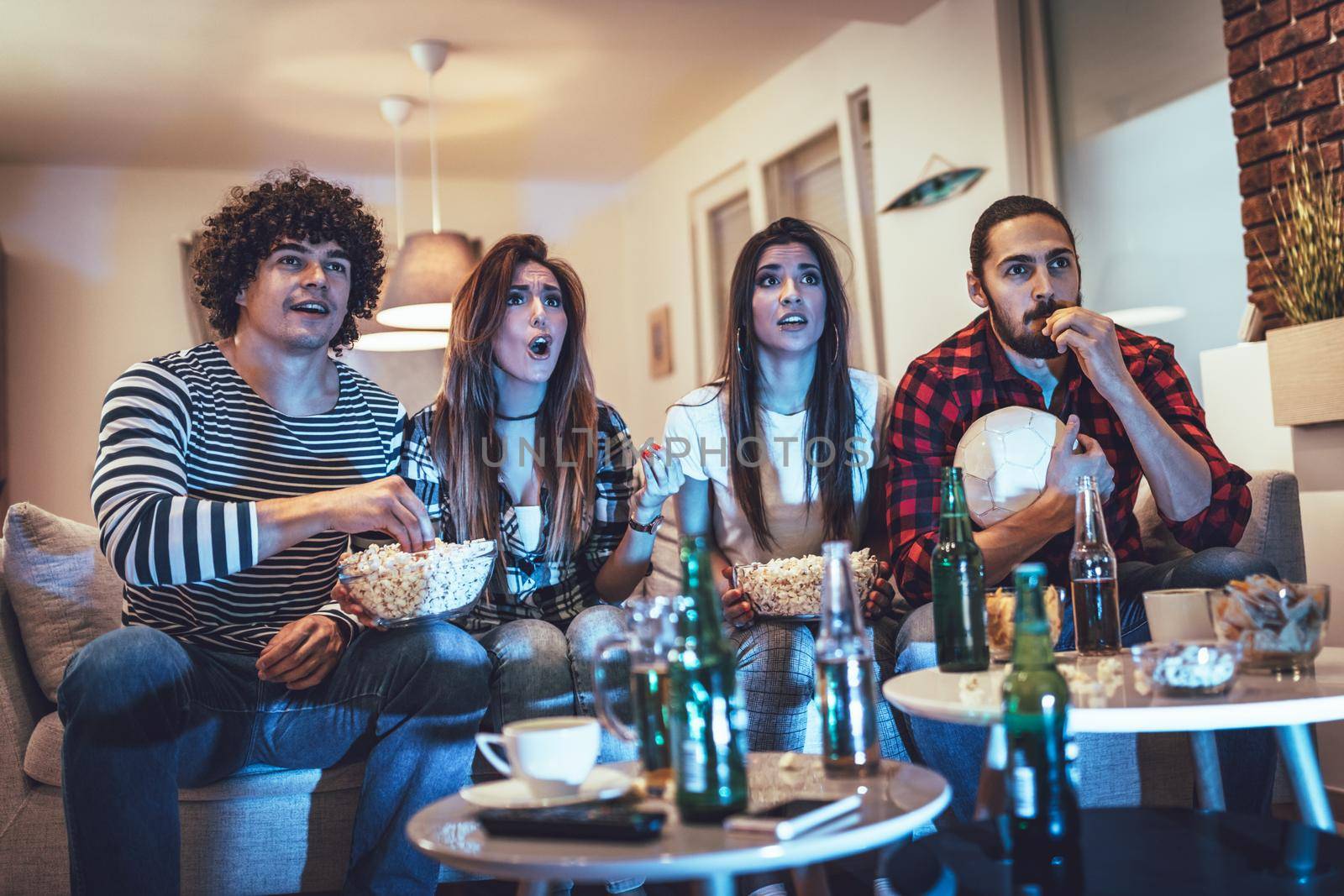 Friends are fans of sports games as football love spending their free time at home together. They are screaming and gesturing for a victory. 