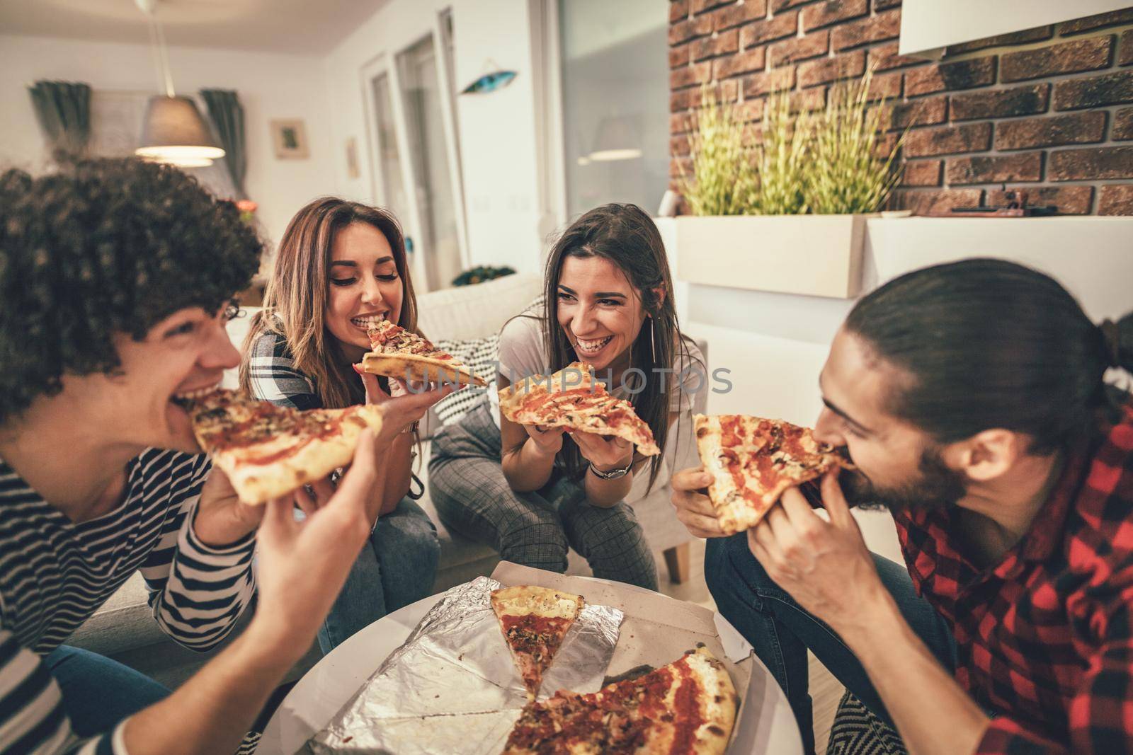 Happy friends having fun while eating pizza. They have great weekend in nice company indoors. 