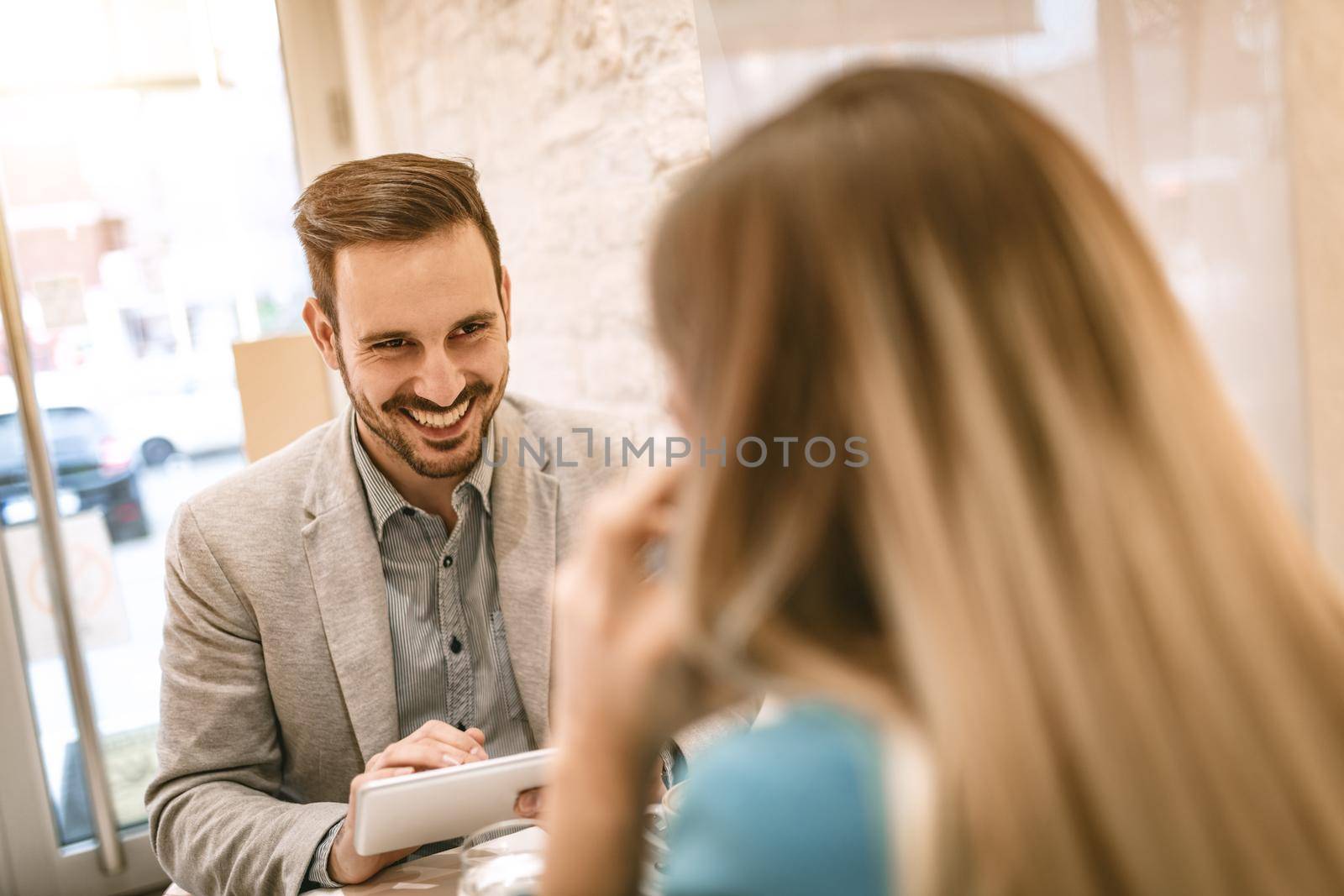 Young businesspeople on a break in a cafe. Woman using smart phone, man working at tablet and flirting with her.