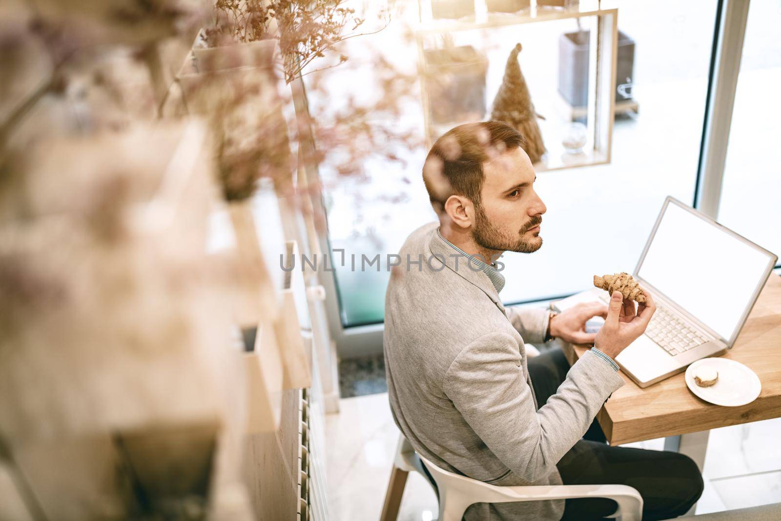 Young businessman on a break in a cafe. He is working at laptop and using having breakfast. 