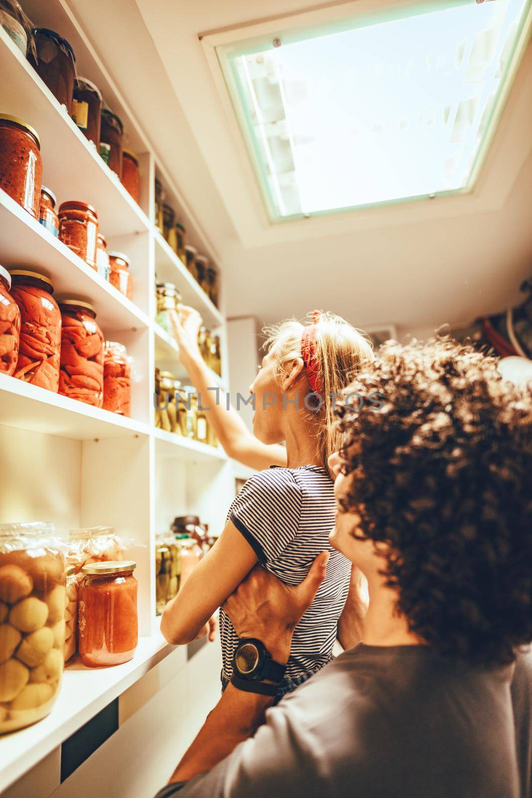 A happy family takes jars with pickled vegetables from the pantry shelf. His father is holding high.