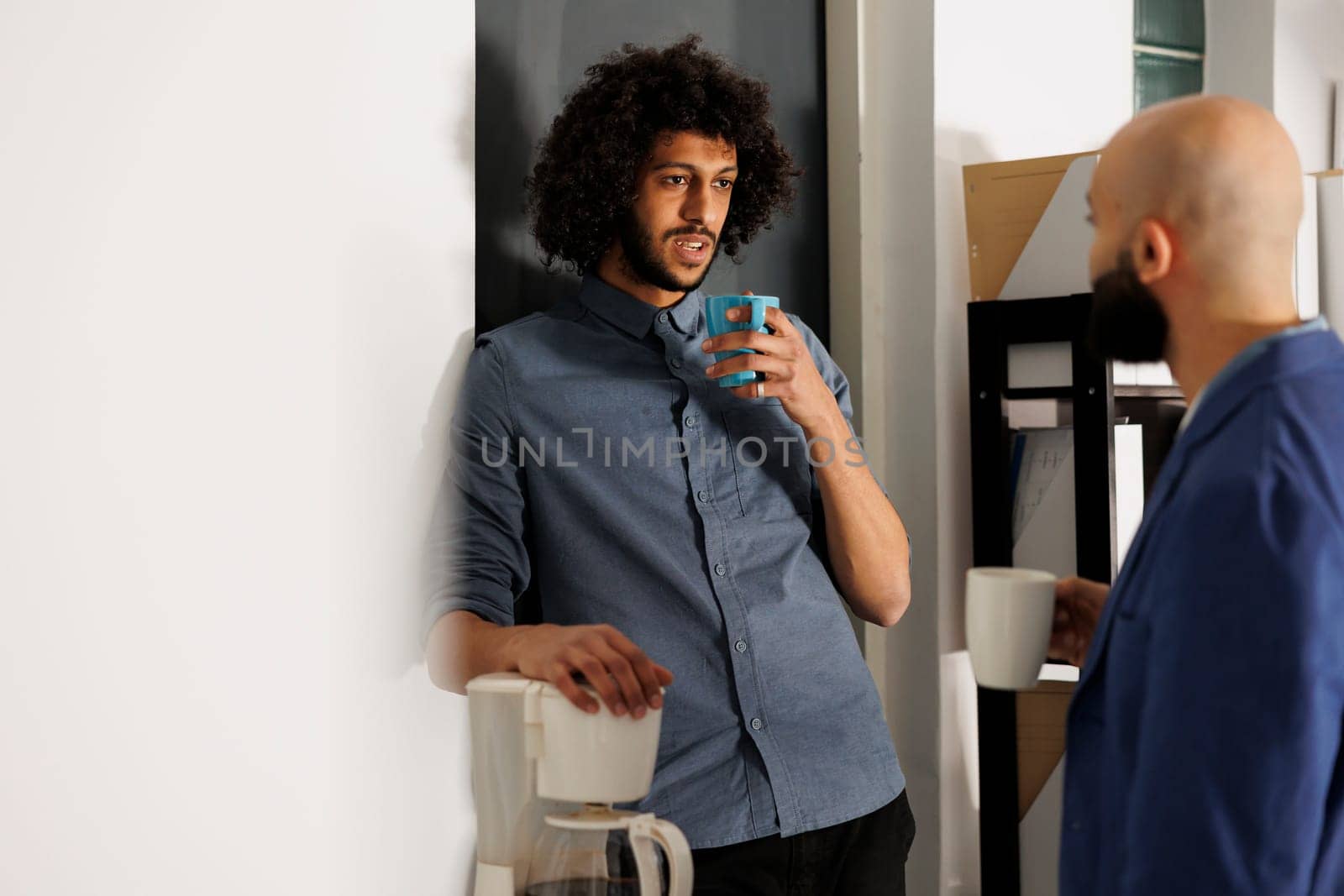 Arab coworkers having conversation while drinking coffee and standing in business office. Two colleagues discussing company start up project during work break in coworking space