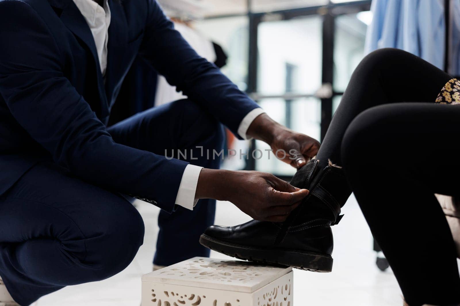 Retail employee helping african american client with purchase in shopping center. Stylish customer trying stylish shoes, buying trendy merchandise in boutique, commercial activity. Close up