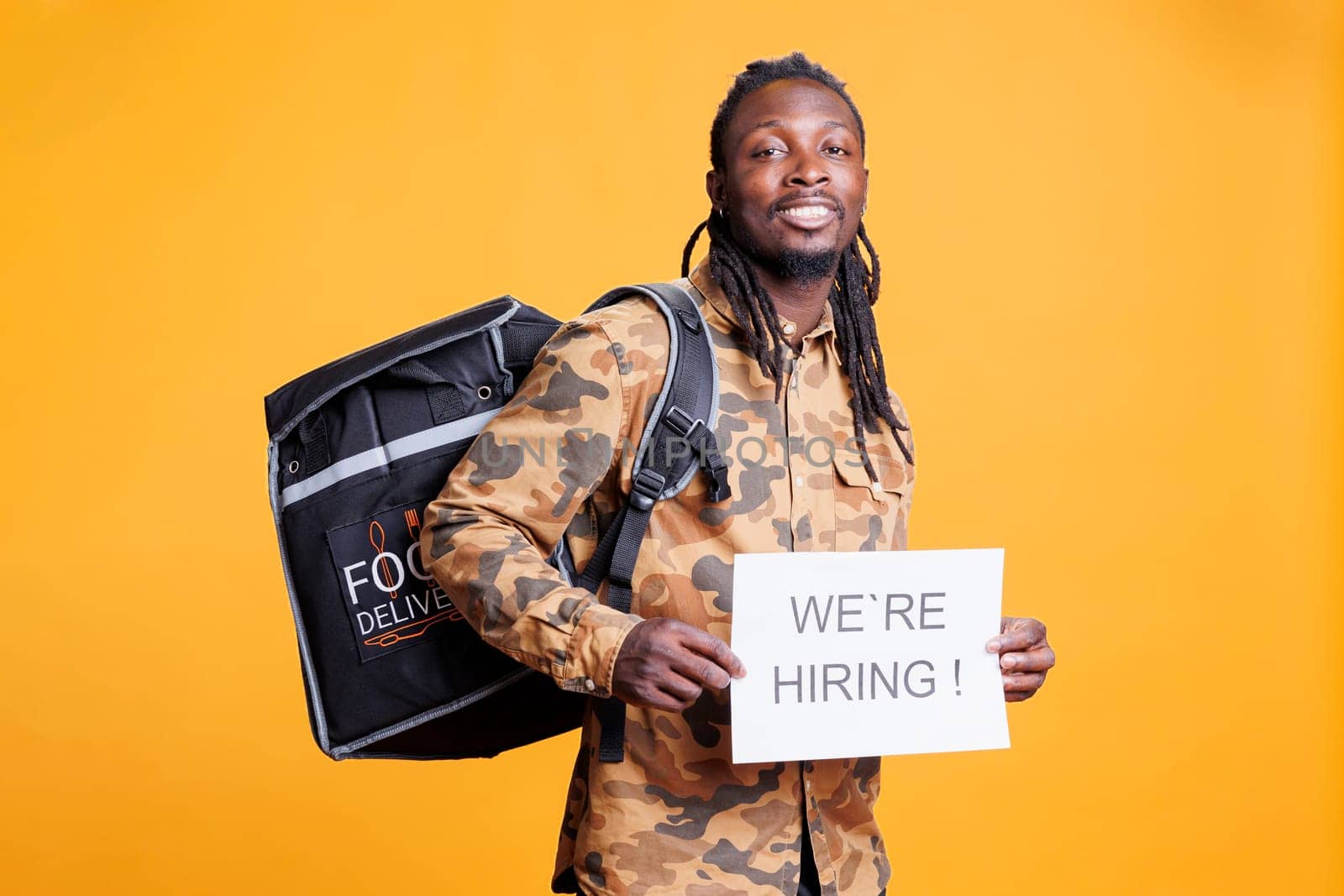 Takeout delivery employee with thermal backpack holding hiring application sign for courier position. African american person wanting perfect candidate for career opportunity in studio