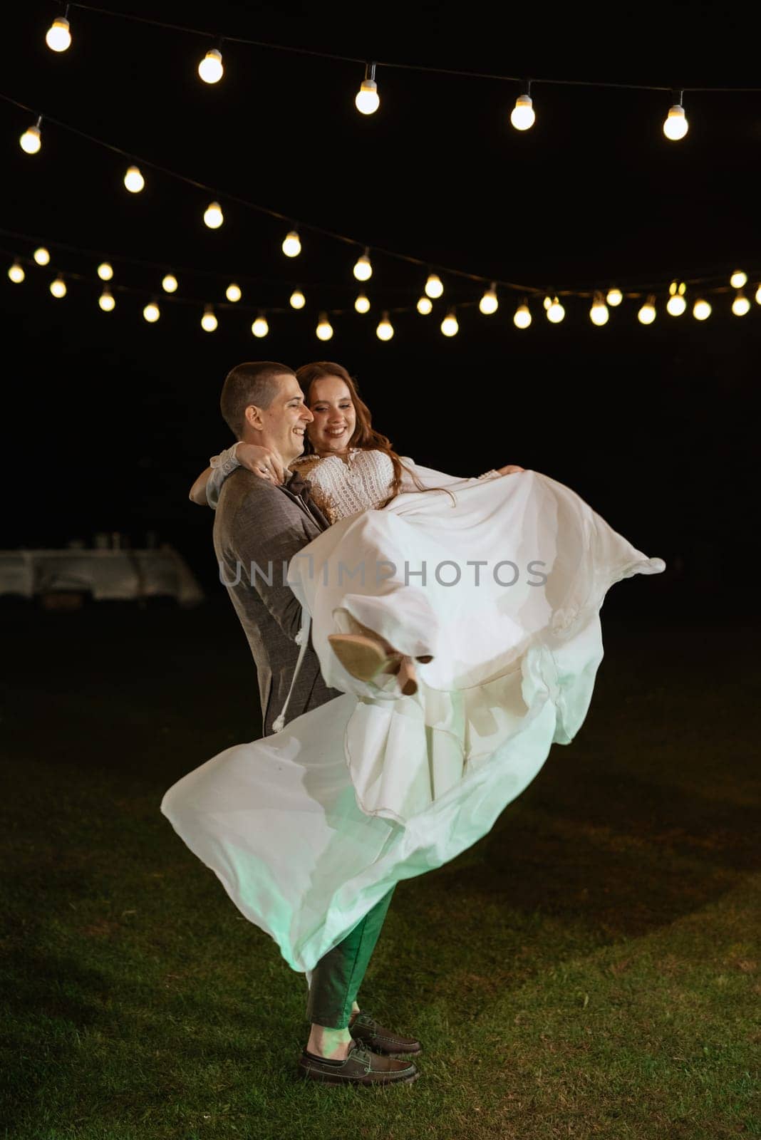 the first wedding dance of the bride and groom in the glade of the country club in the light of sunset and warm garlands