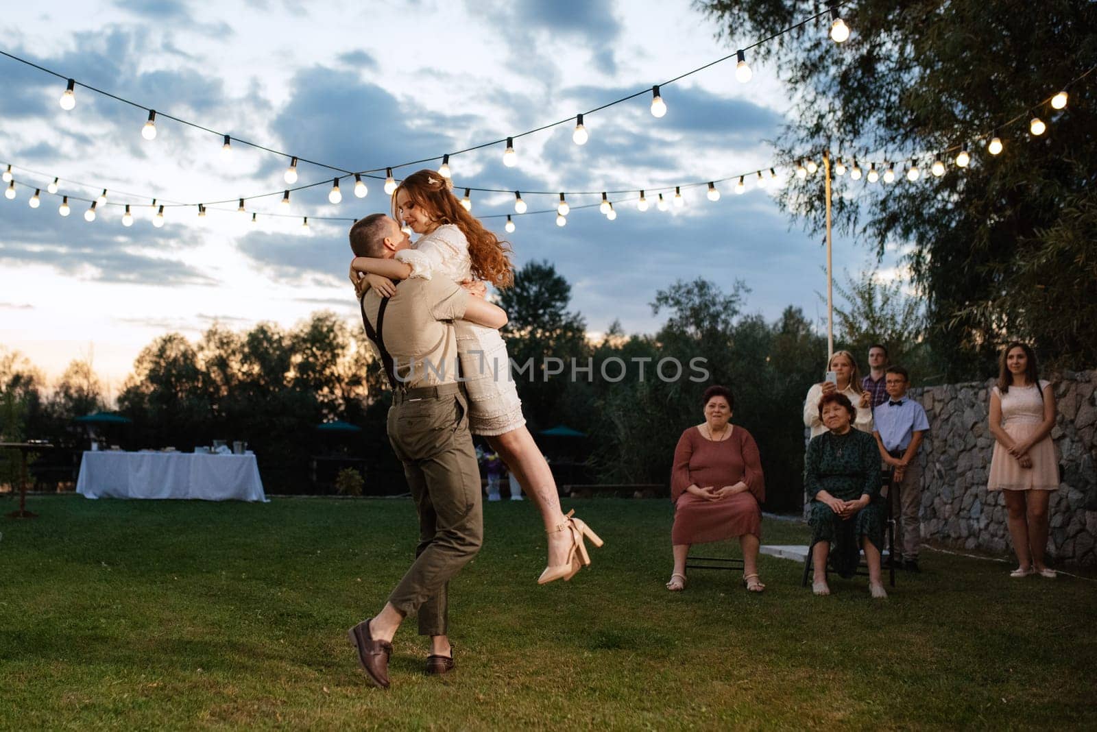 the first wedding dance of the bride and groom in the glade of the country club in the light of sunset and warm garlands