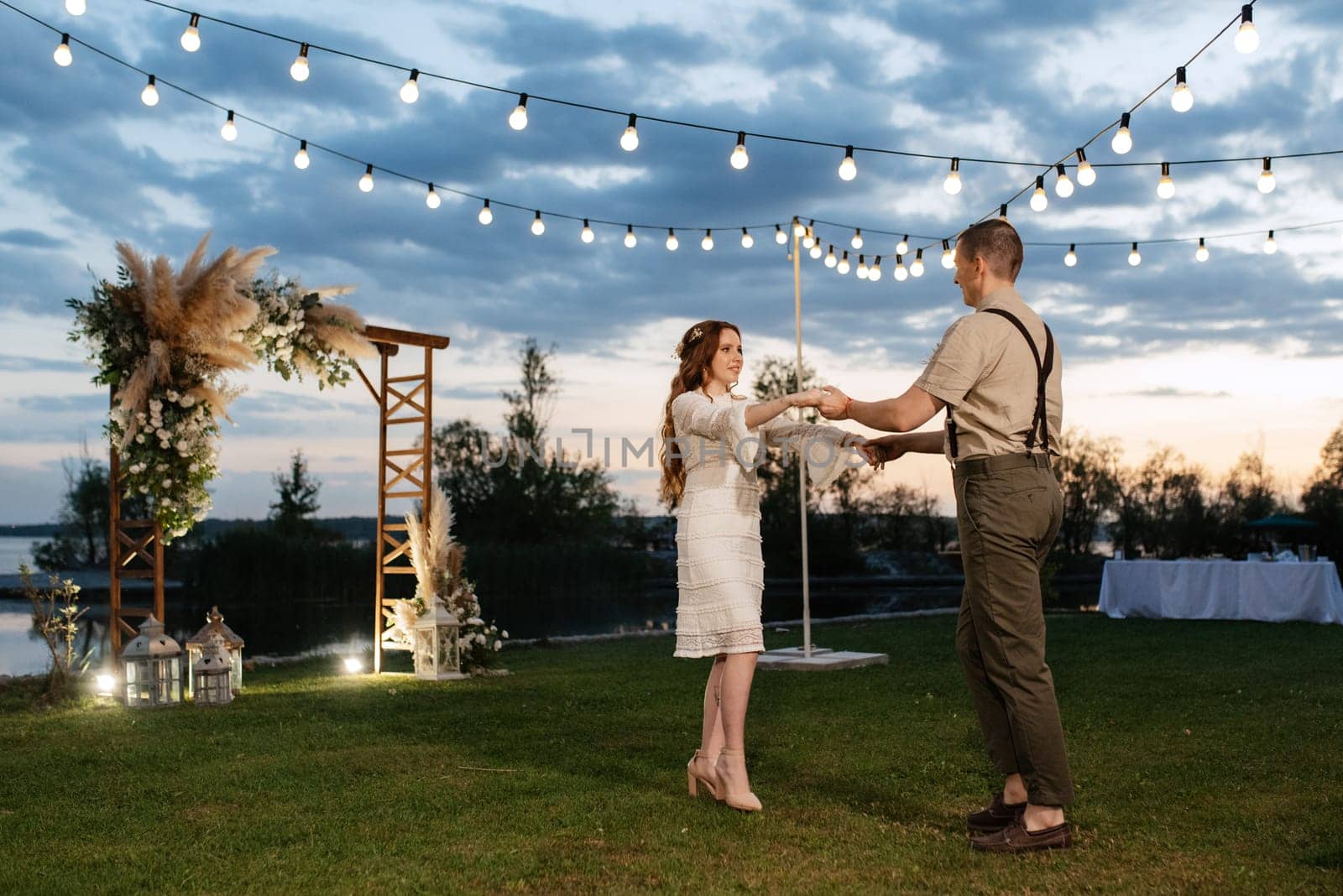 the first wedding dance of the bride and groom in the glade of the country club in the light of sunset and warm garlands