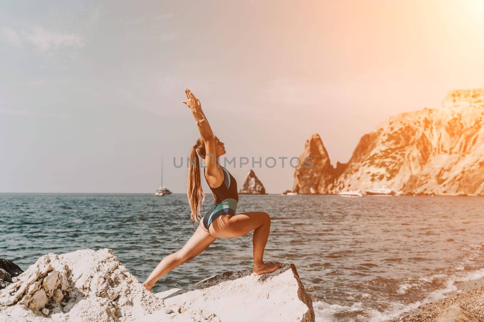 Yoga on the beach. A happy woman meditating in a yoga pose on the beach, surrounded by the ocean and rock mountains, promoting a healthy lifestyle outdoors in nature, and inspiring fitness concept