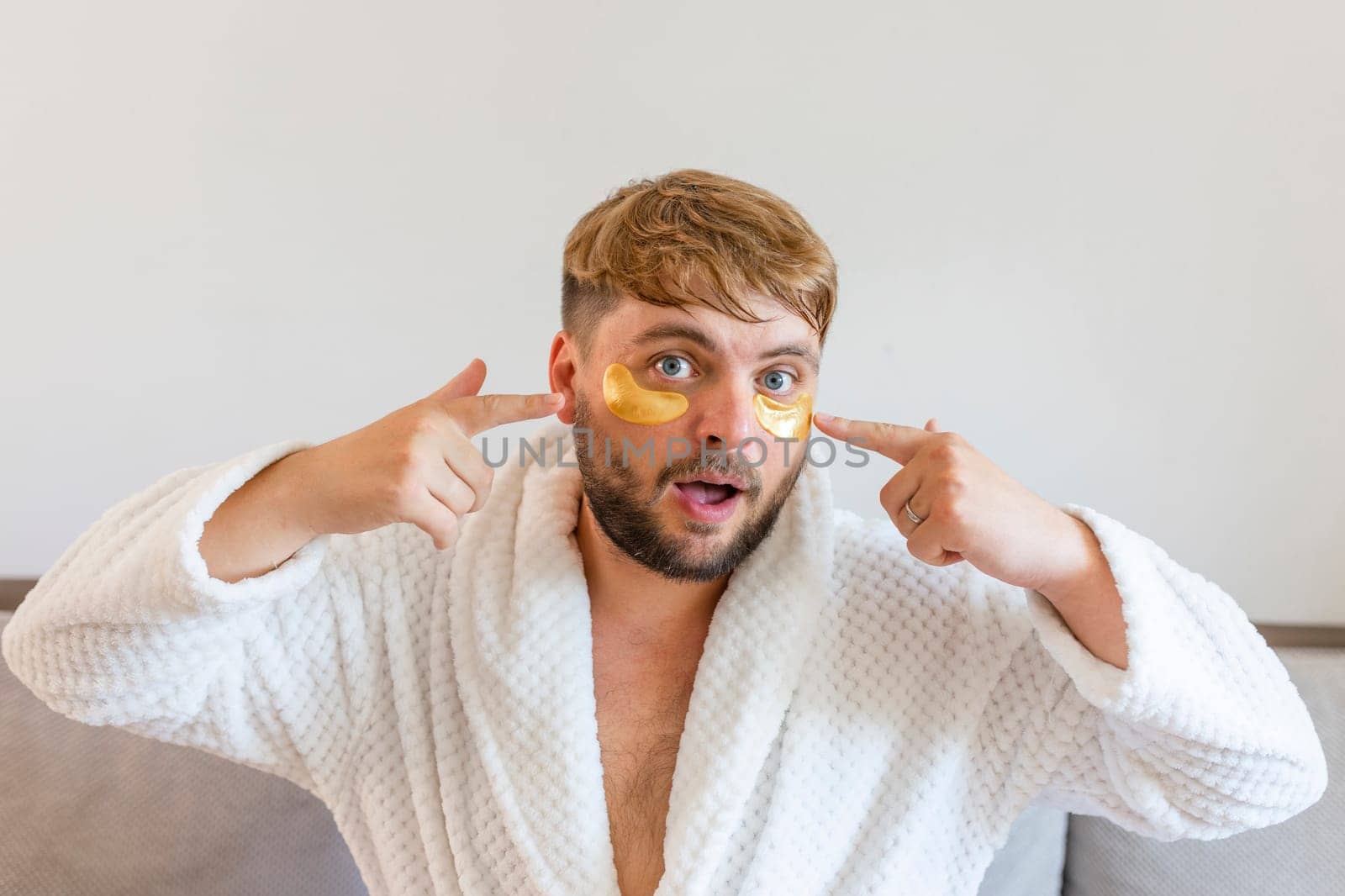 Beauty treatments, skin care, metrosexual concept. A handsome bearded man with golden bandages under his eyes makes funny faces with facial expressions.