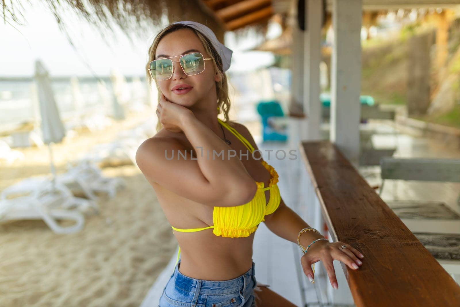 Sexy girl in sunglasses and swimsuits posing near beach bar.