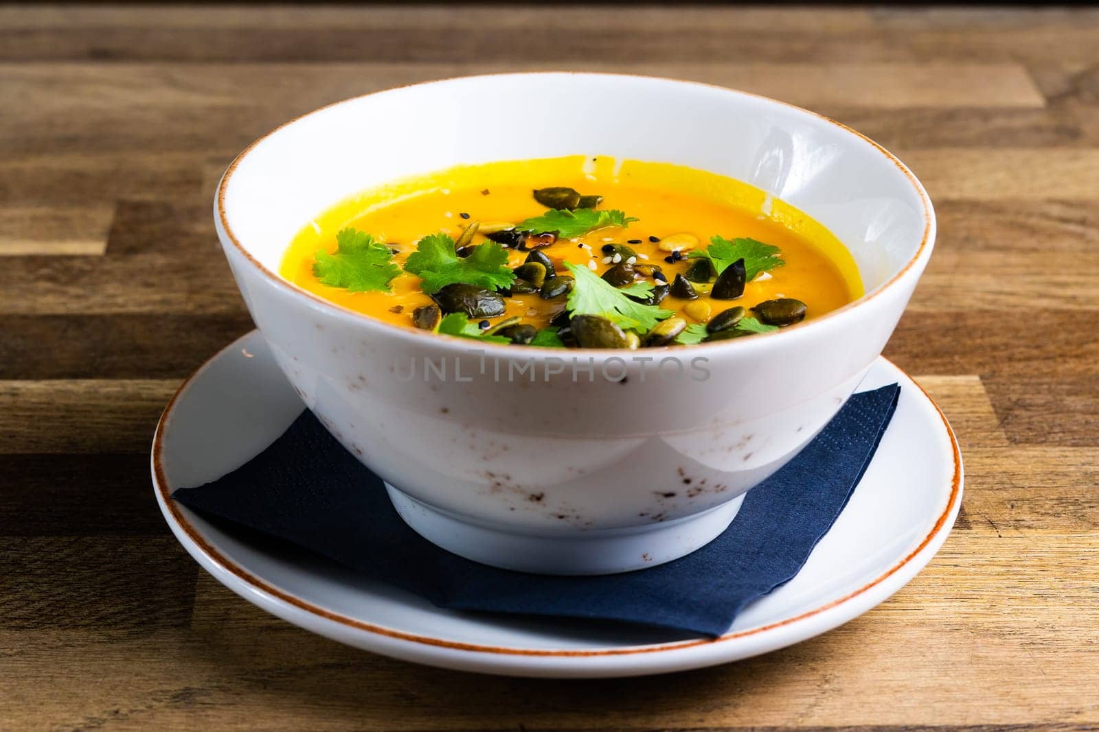 Pumpkin and carrot soup with cream and parsley on a dark wooden background