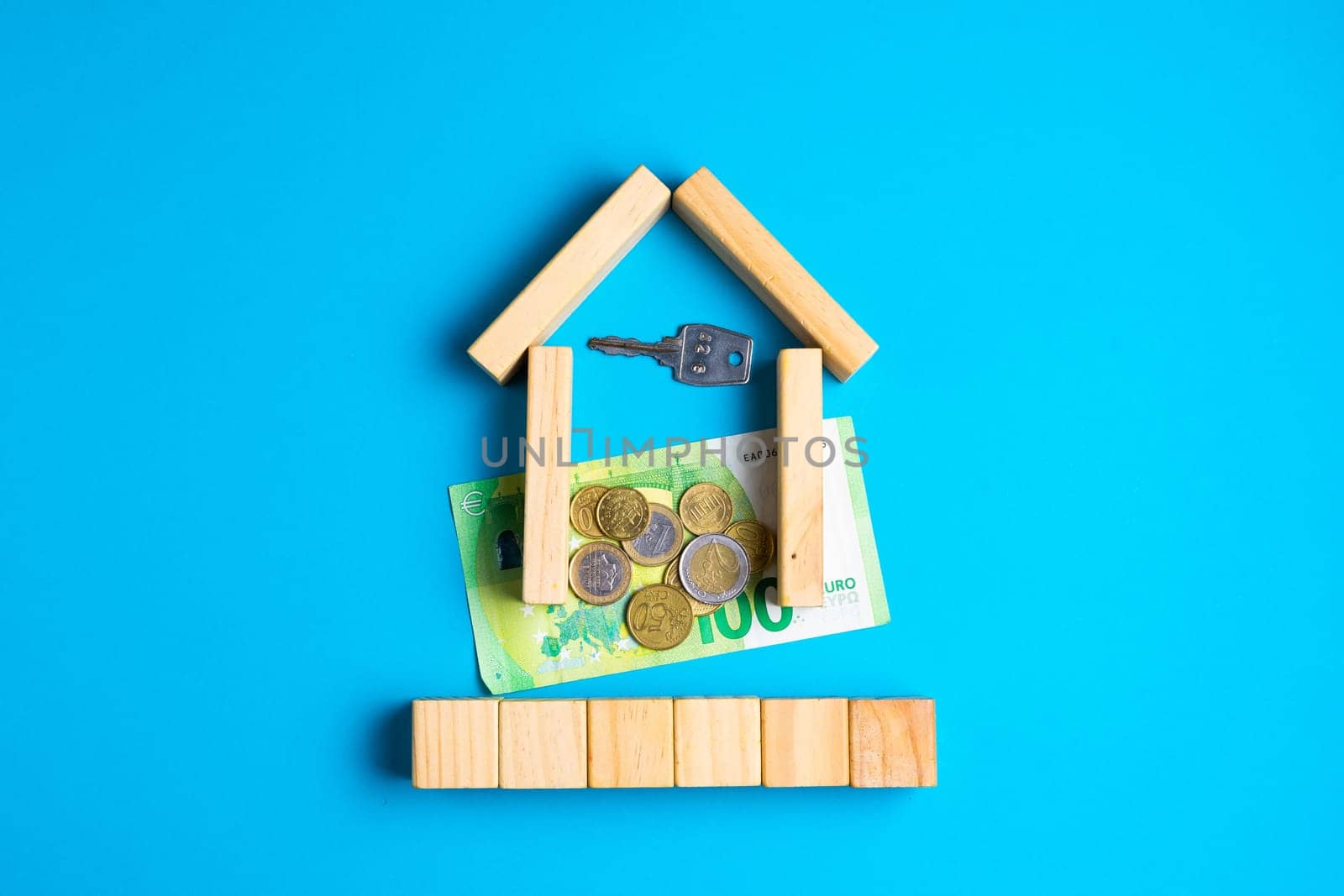 Wooden house model with coins, key, money, copy space on blue background.