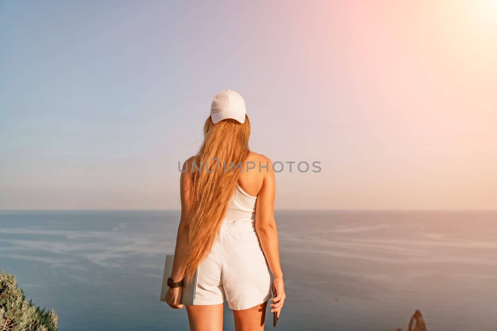 A female tourist stands by the sea wearing a white cap and T-shirt, looking happy and relaxed