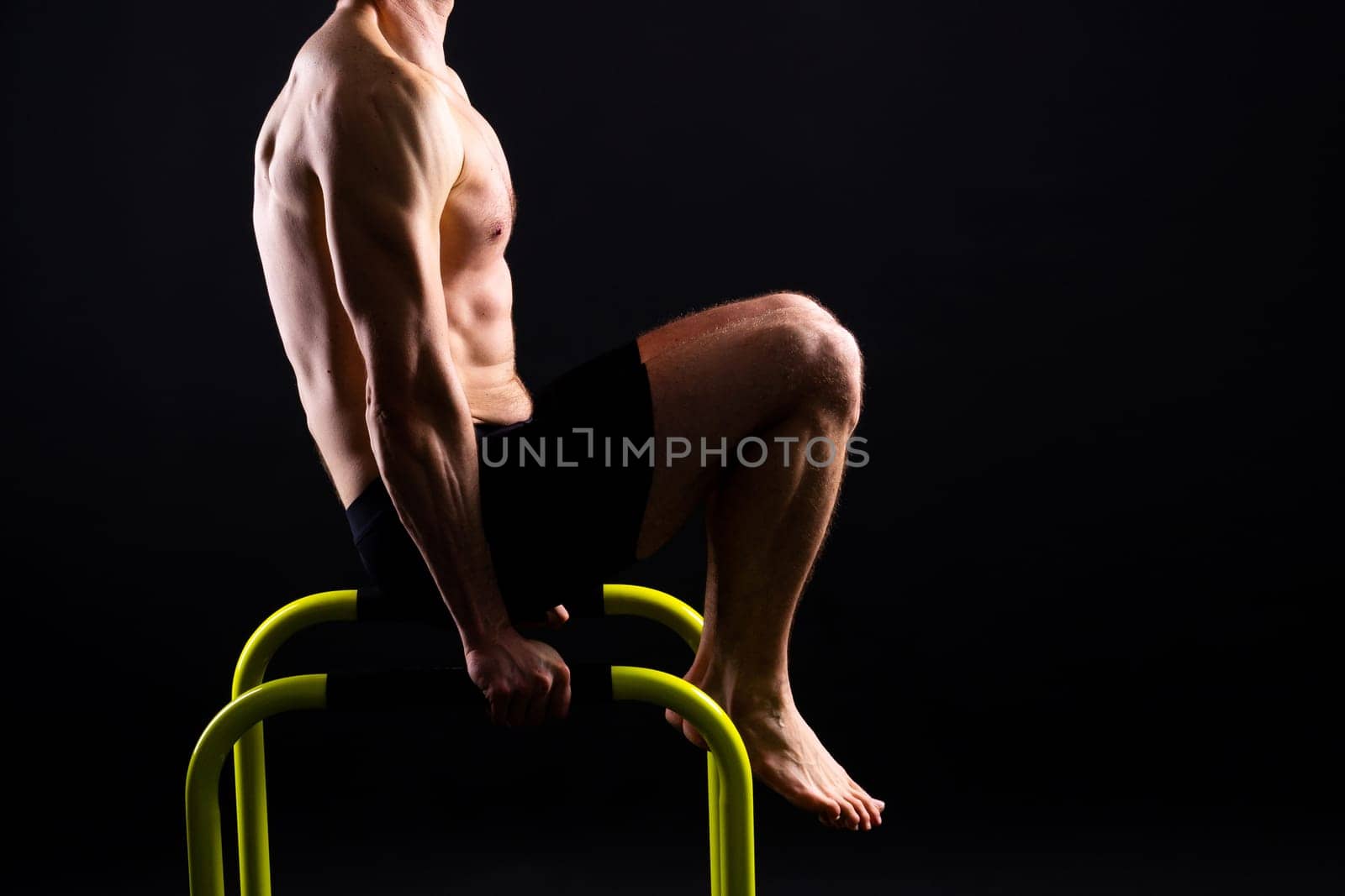Young muscular man doing parallel bar exercises in a dark white red studio with copy space