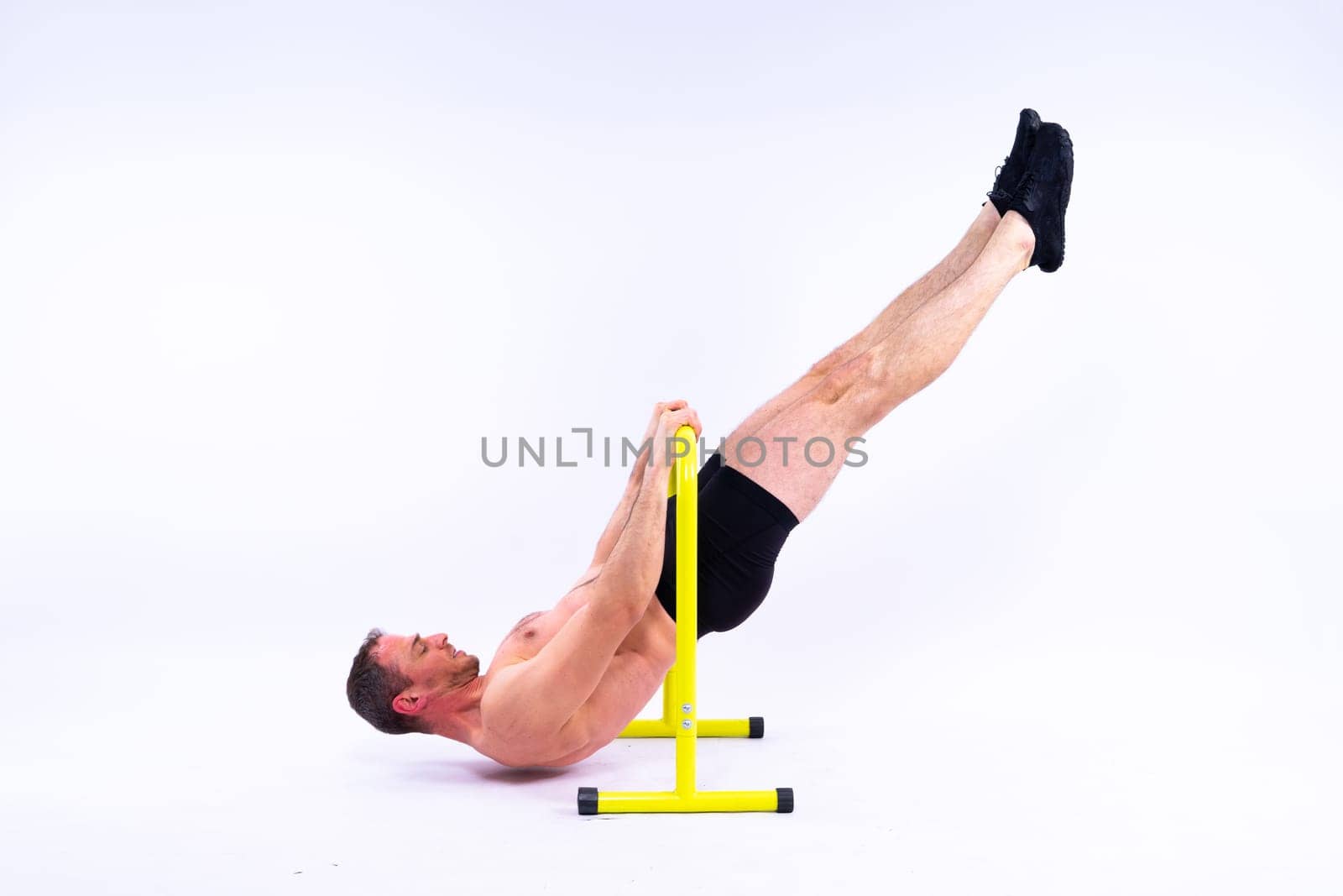 Young muscular man doing parallel bar exercises in a dark white red studio with copy space