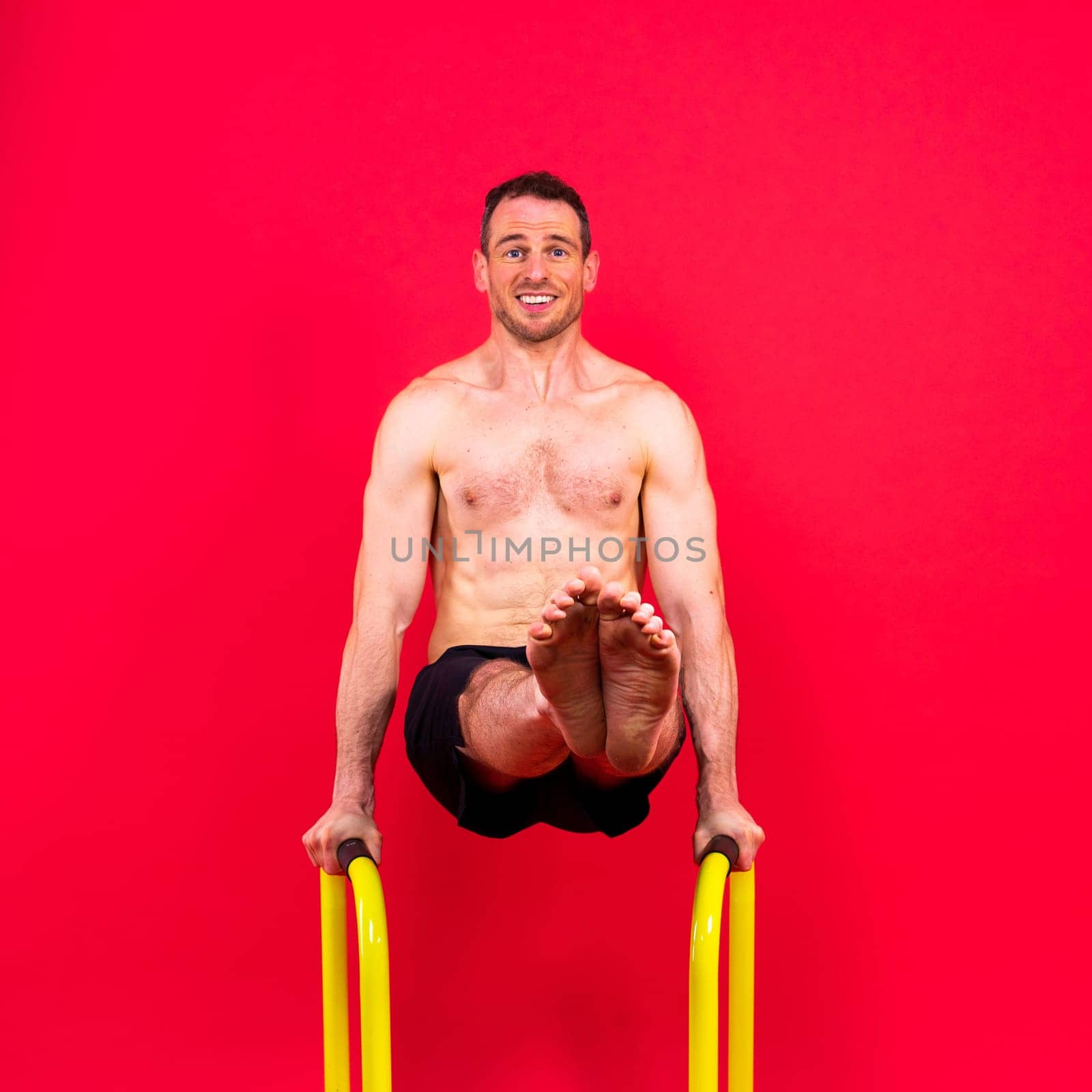 Young muscular man doing parallel bar exercises in a dark white red studio with copy space