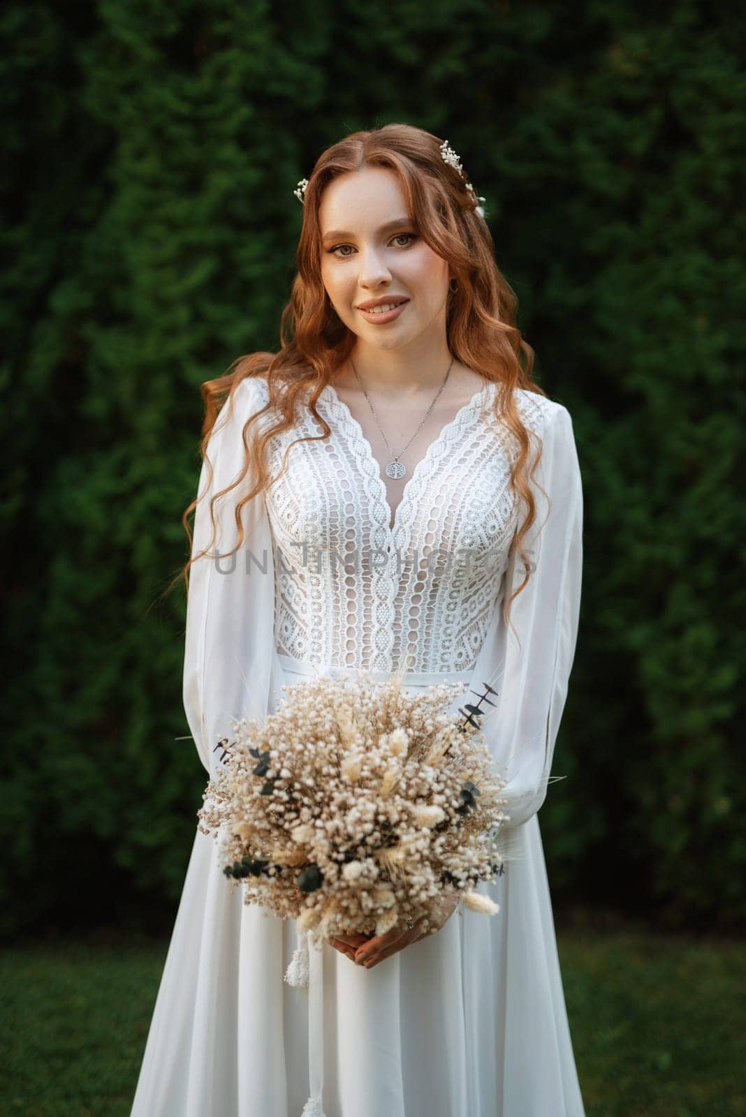 red-haired girl bride with a wedding bouquet on a meadow with green thuja