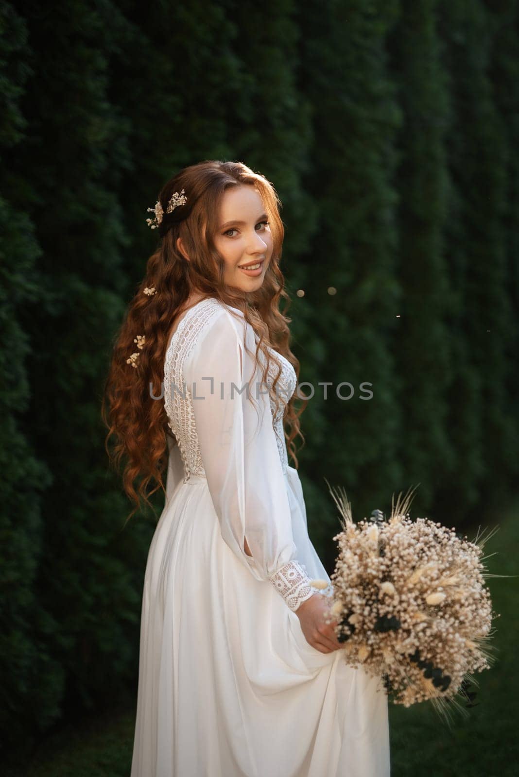 red-haired girl bride with a wedding bouquet on a meadow with green thuja