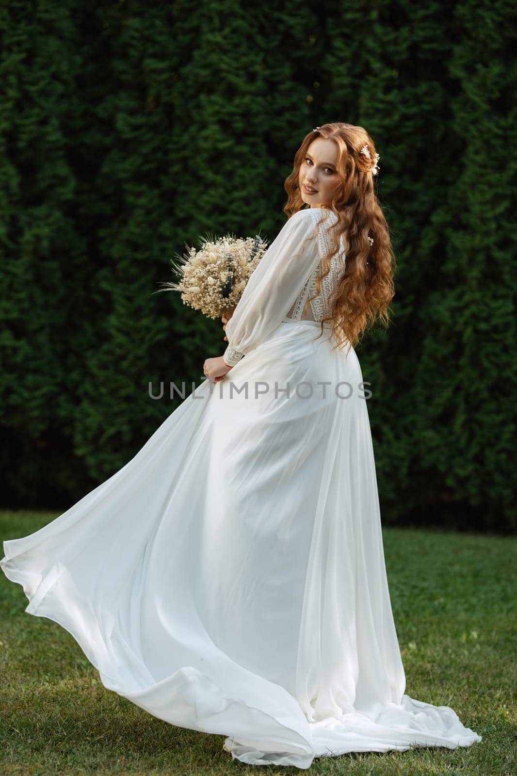 red-haired girl bride with a wedding bouquet on a meadow with green thuja