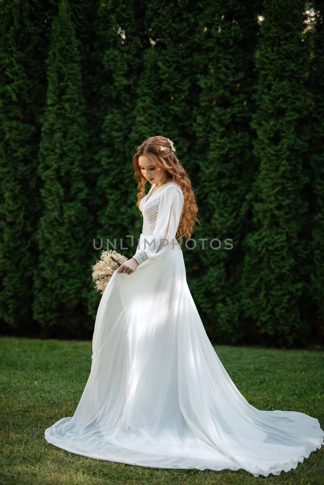 red-haired girl bride with a wedding bouquet on a meadow with green thuja