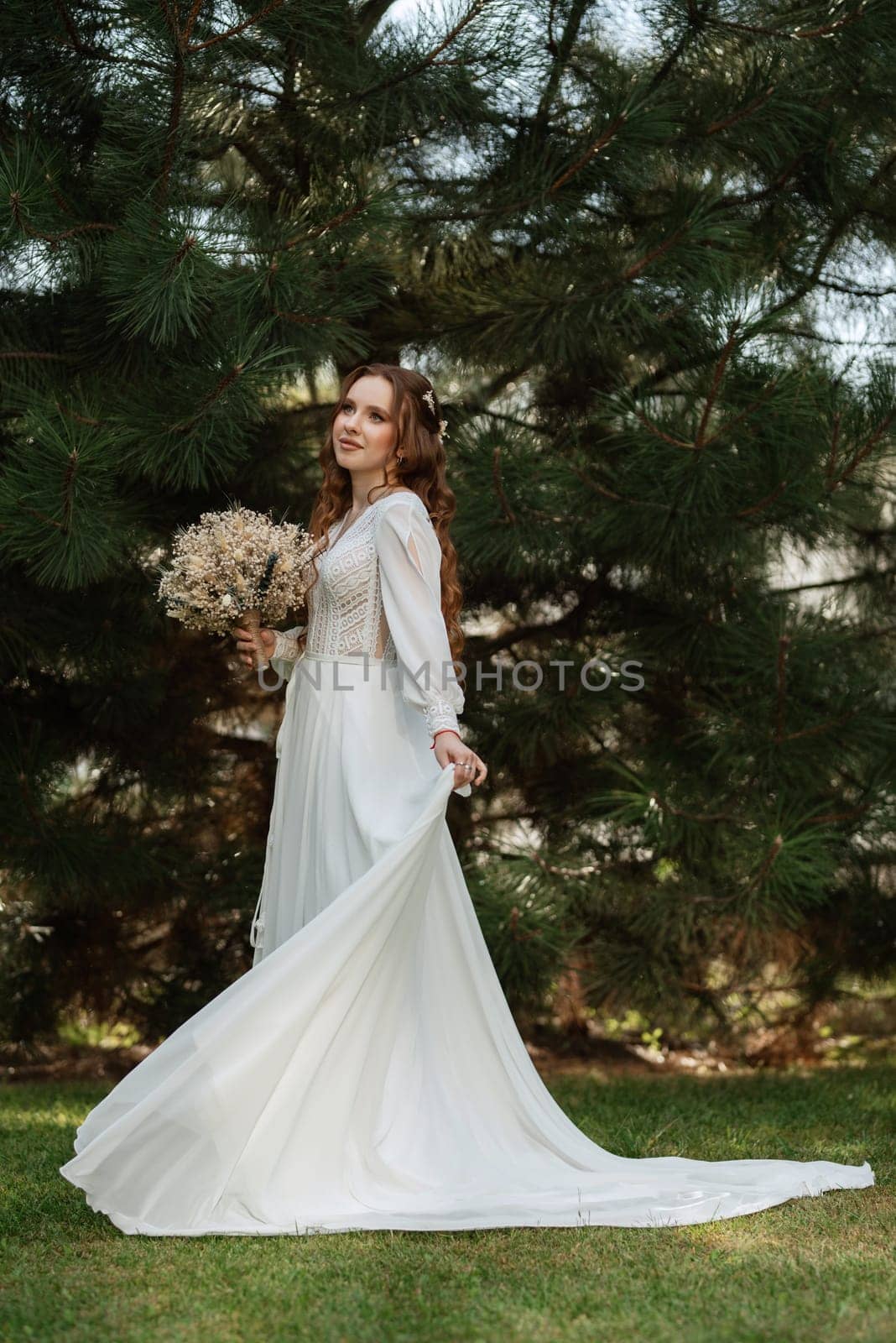 red-haired girl bride with a wedding bouquet on a meadow with green thuja