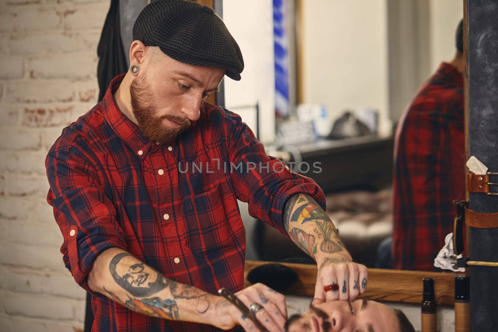 Client with beard and moustache sit on chair, and professional barber make beard shaving in barber shop