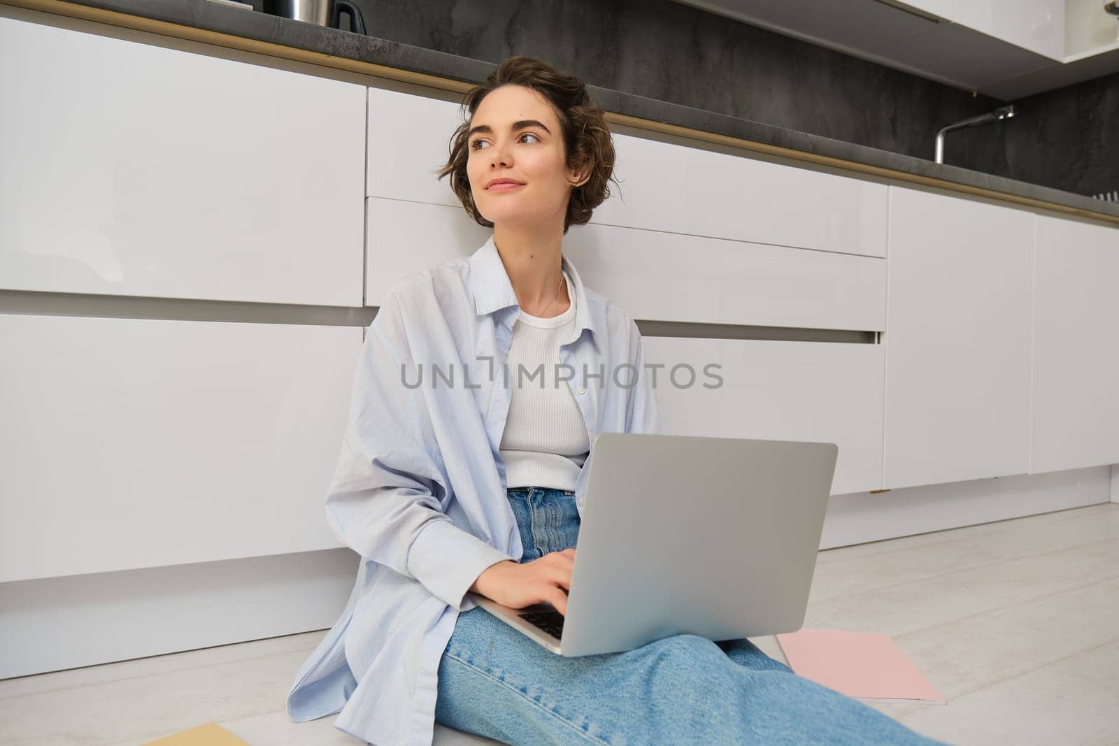 Young IT girl, woman works freelance from home, sits on floor with laptop. Girl student does homework online, writes on computer keyboard.