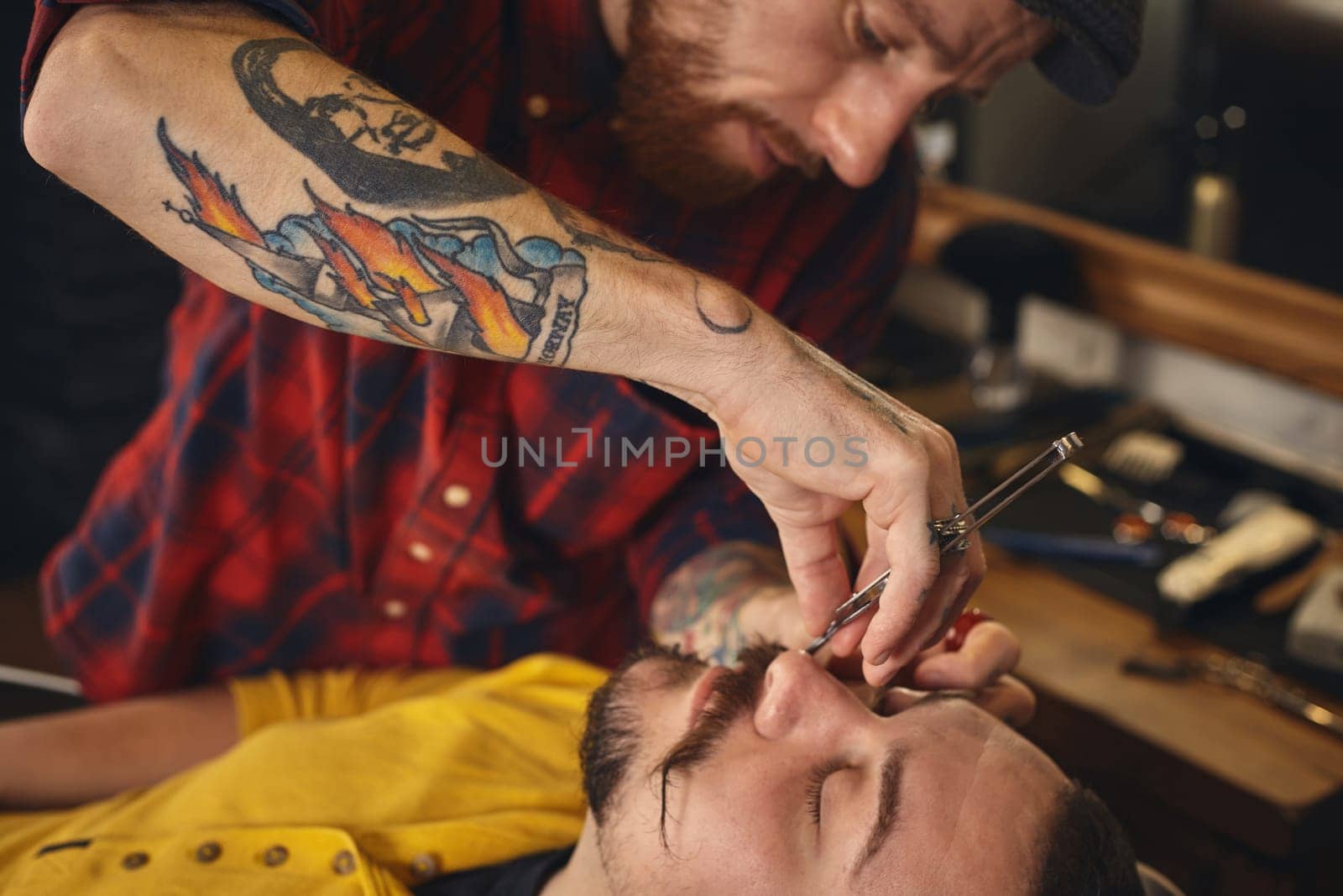 Client with beard and moustache sit on chair, and professional barber make beard shaving in barber shop