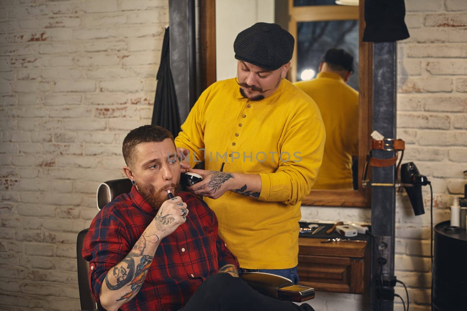 Barber with mustache making haircut of attractive bearded man in barbershop with trimmer
