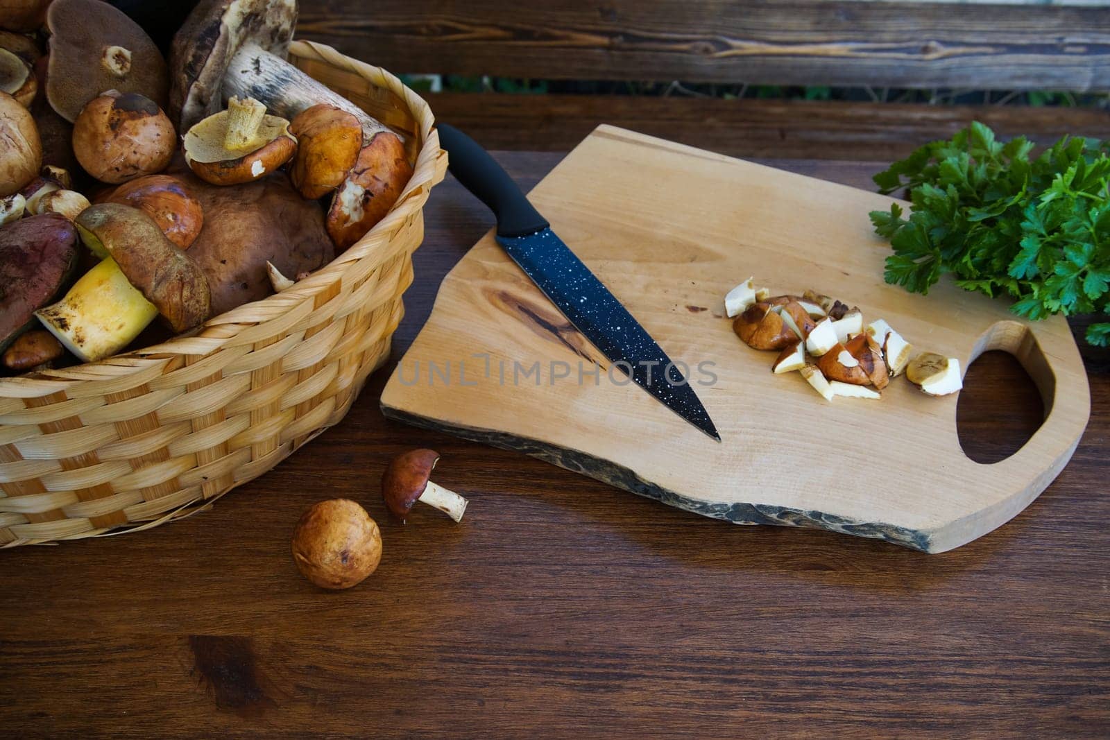 preparation of forest edible mushrooms. There is a basket of mushrooms on the table, there is a cutting board and there are fresh greens