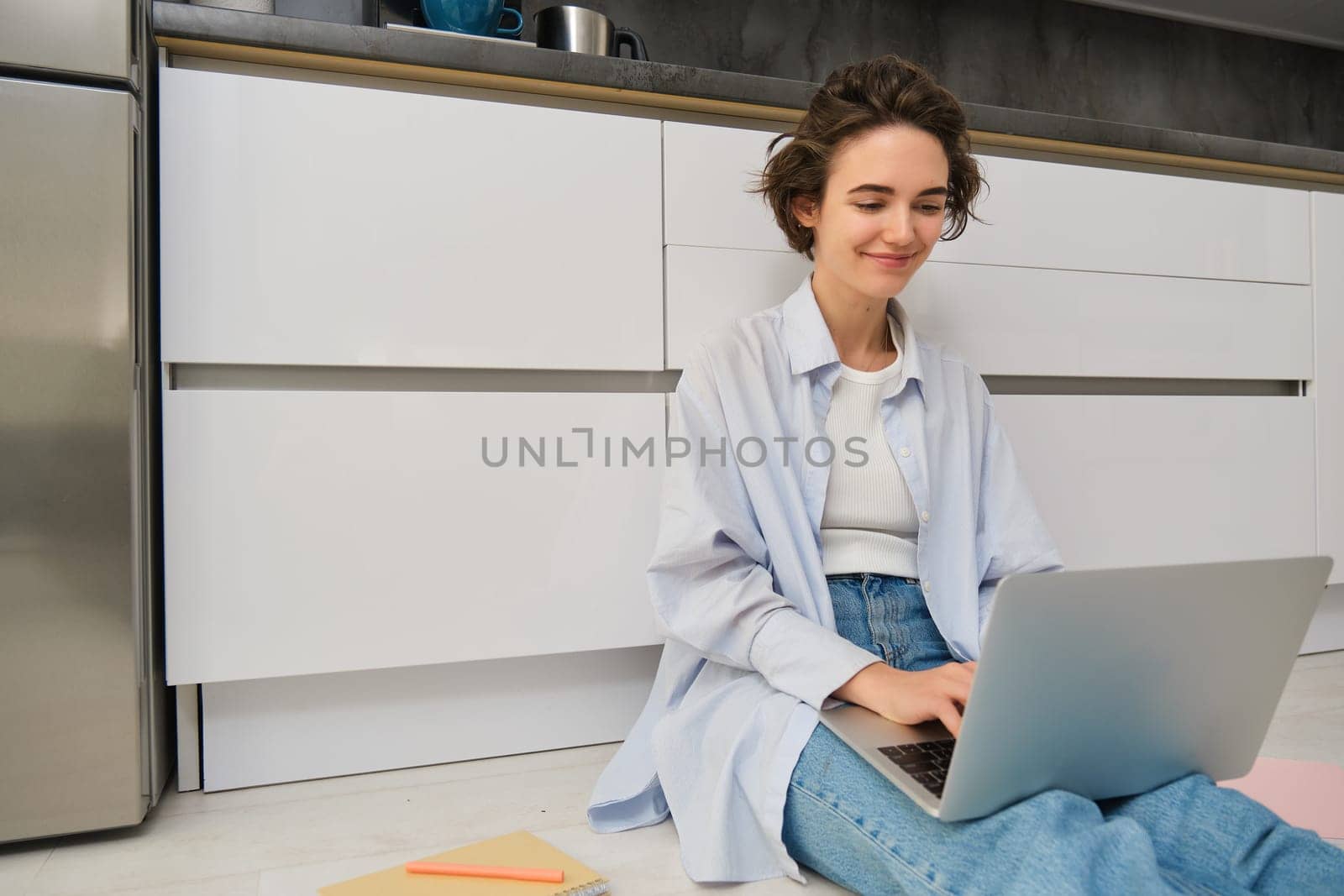 Young IT girl, woman works freelance from home, sits on floor with laptop. Girl student does homework online, writes on computer keyboard.