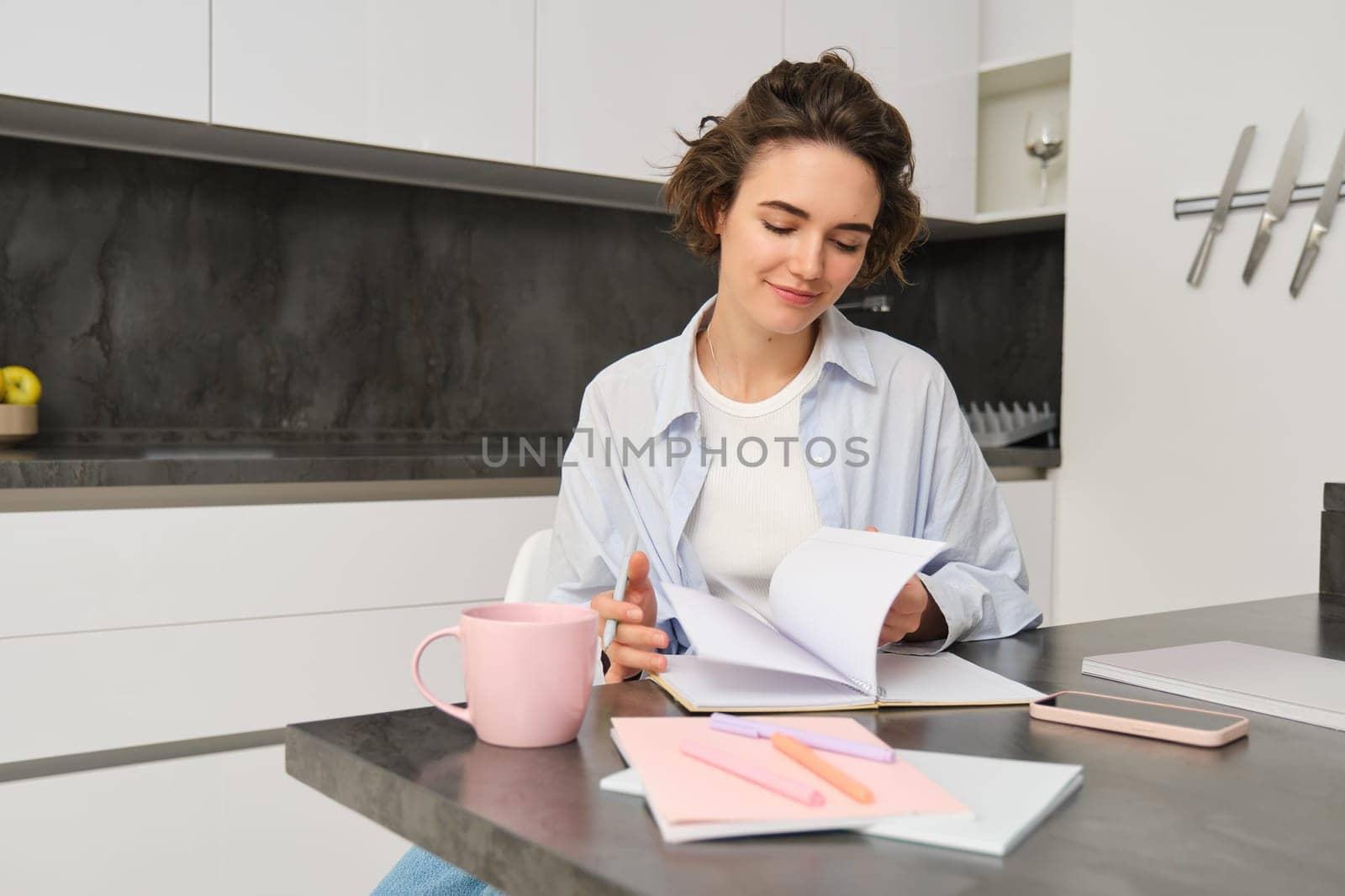 Portrait of young woman at home, working, writing in notebook, taking notes or doing homework.