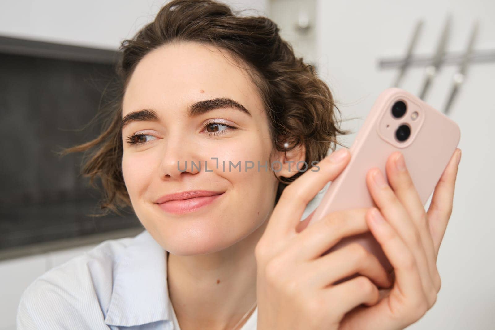 Close up portrait of smiling brunette woman using smartphone, holding mobile phone in hands and looking away, concept of takeaway order, online shopping and communication.