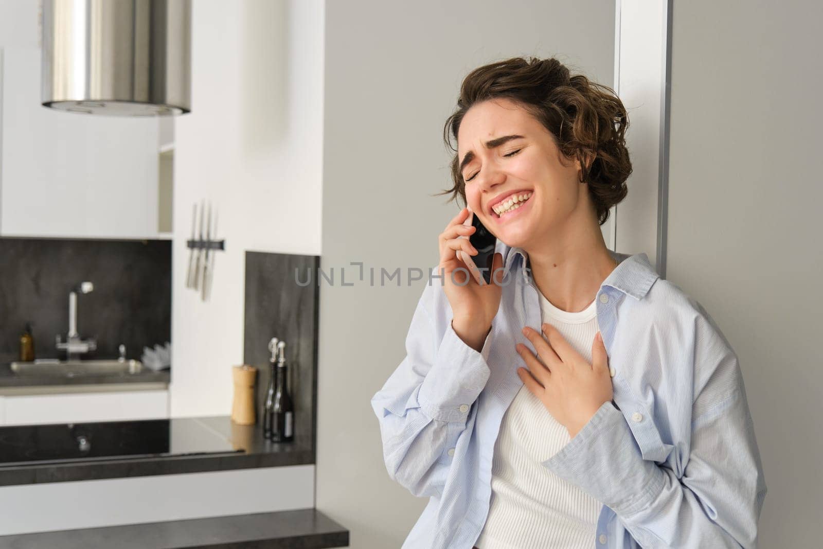 Happy woman talking on mobile phone, laughing and smiling with eyes closed, having nice friendly conversation over telephone.