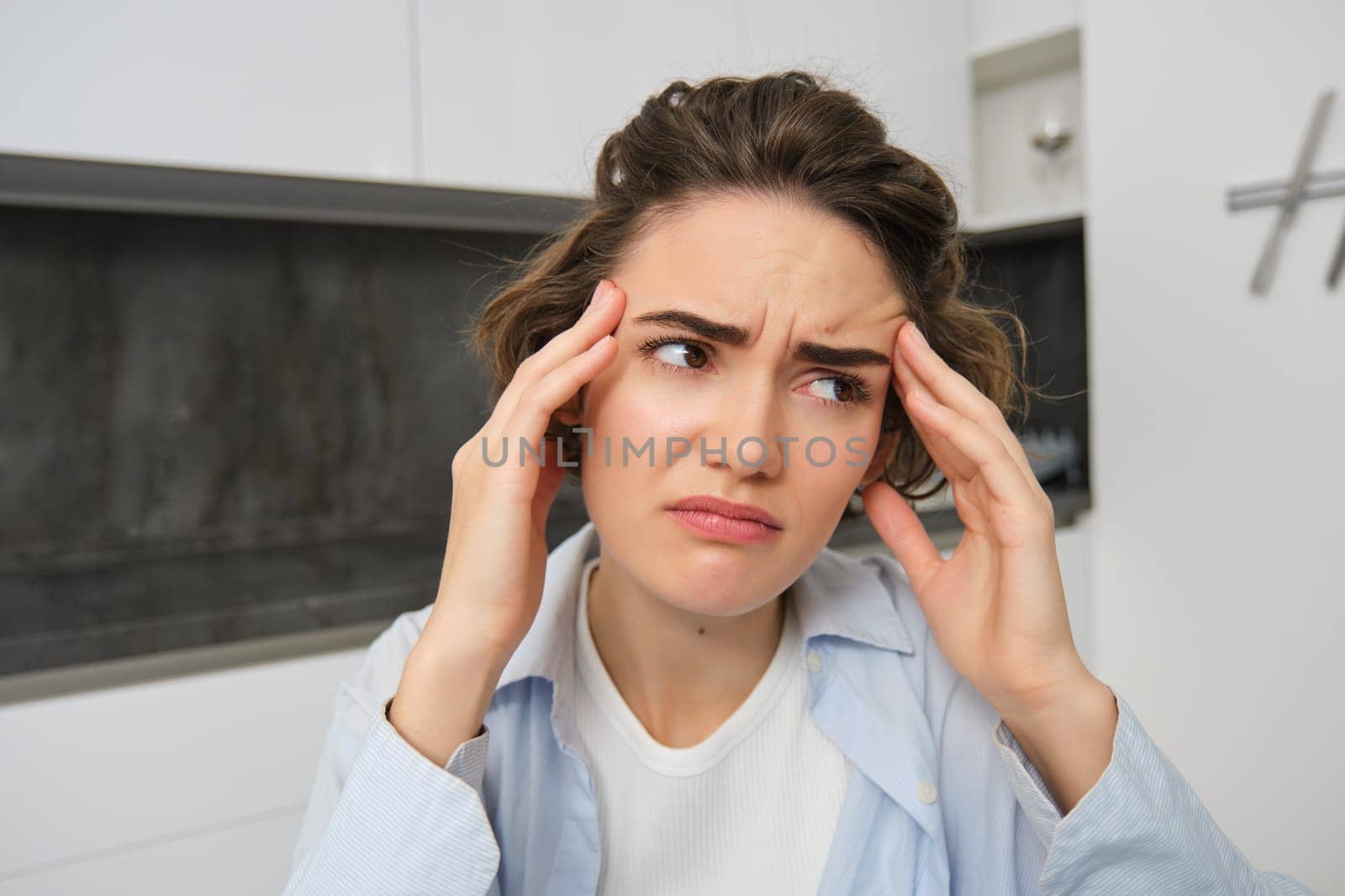 Portrait of brunette woman touches her head, grimaces from pain, has headache, painful migraine.