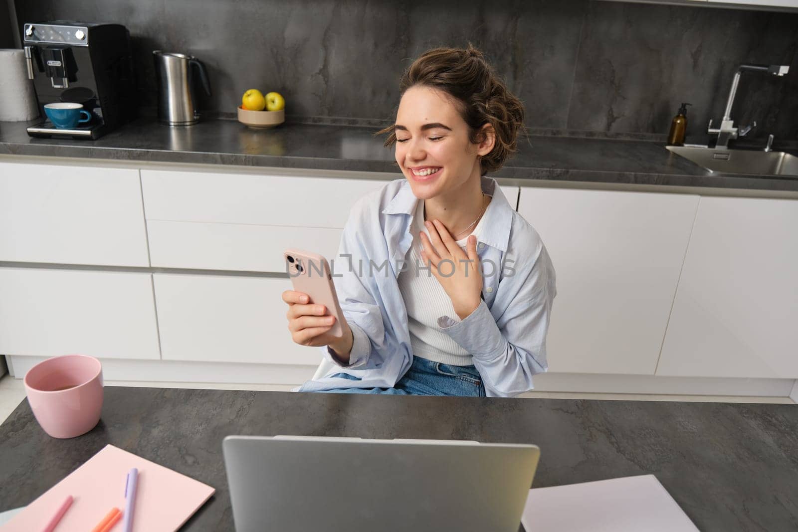 Portrait of candid young woman, laughing, using laptop and smartphone, video chats, joing online conversation, team meeting from home.