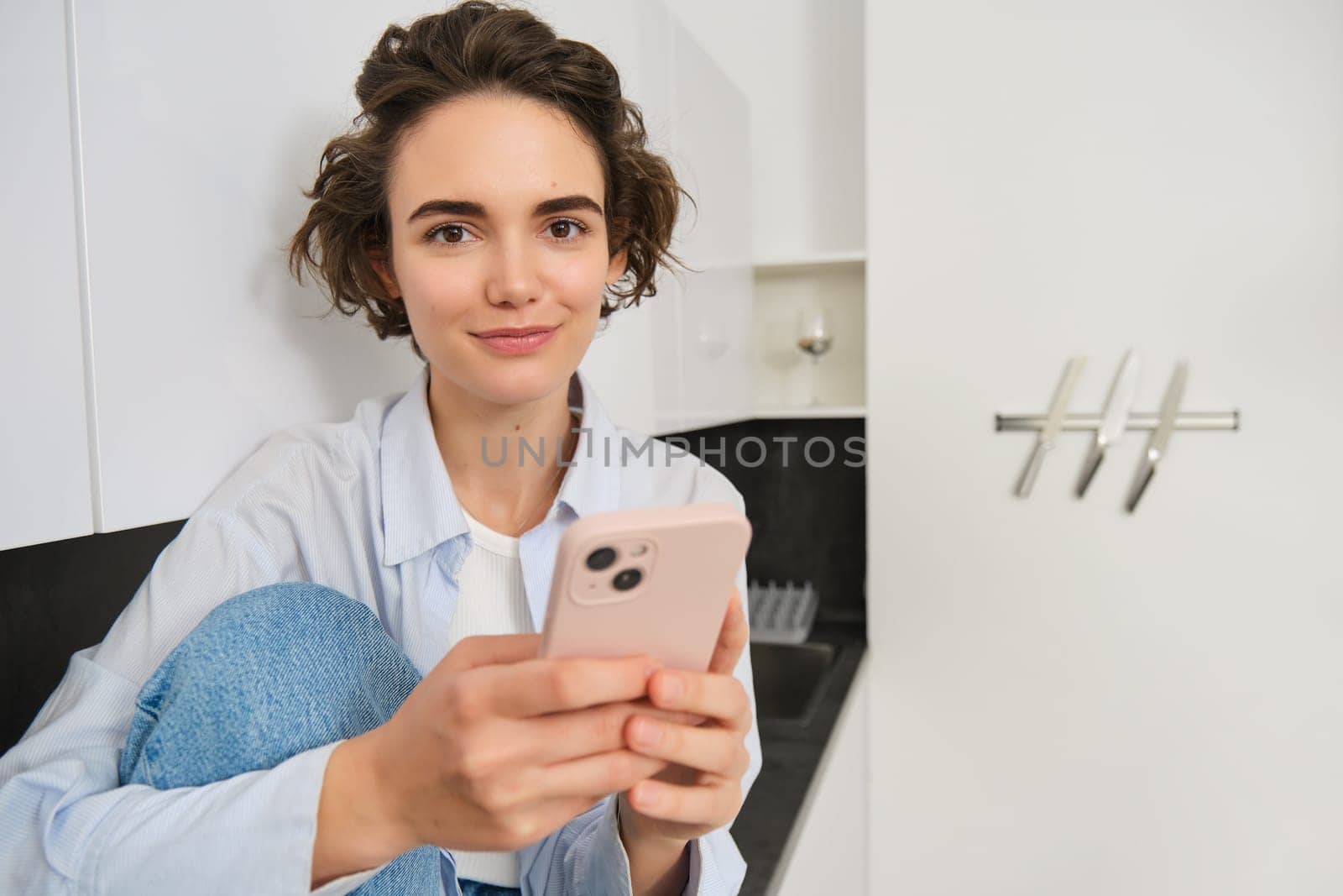 Smiling brunette girl sitting with smartphone at home, orders takeaway from mobile phone app, using online shopping application.