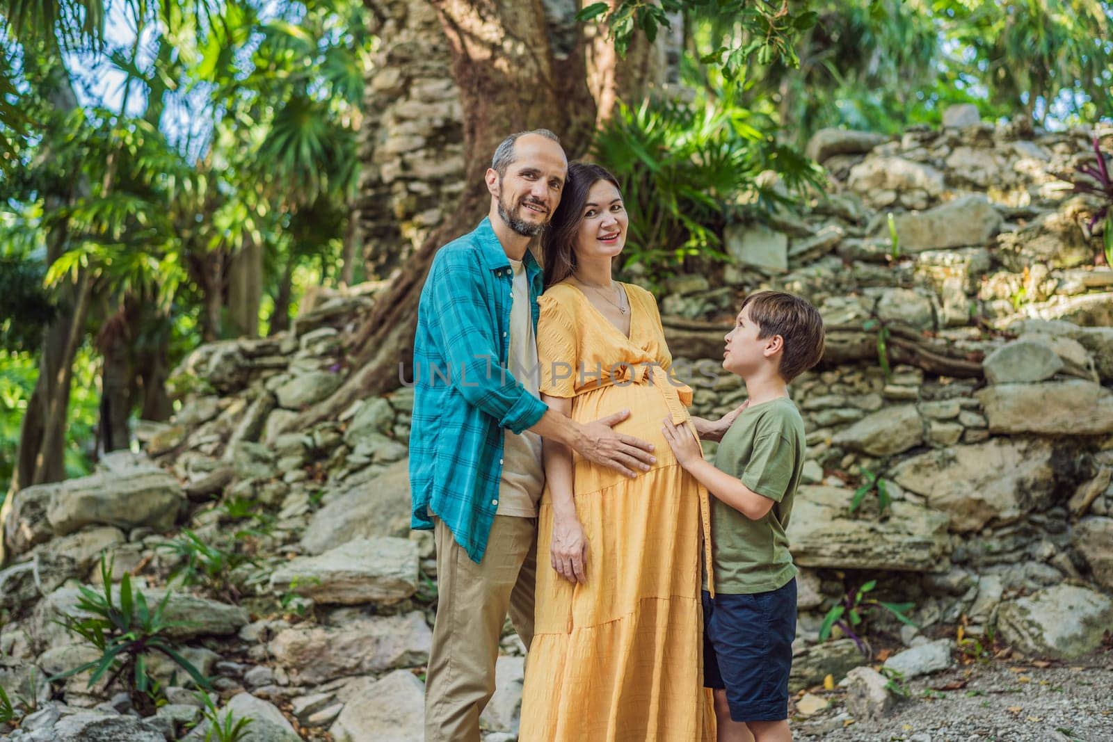 A loving family enjoying a leisurely walk in the park - a radiant pregnant woman after 40, embraced by her husband, and accompanied by their adult teenage son, savoring precious moments together amidst nature's beauty. Pregnancy after 40 concept by galitskaya