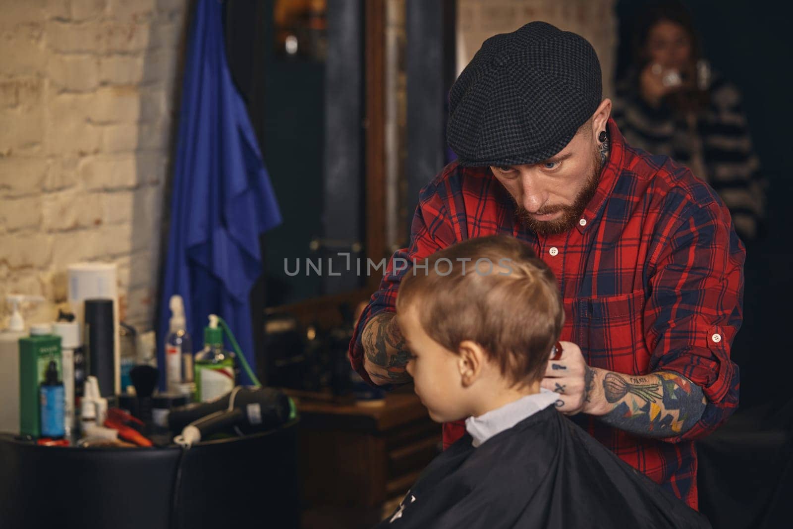 A pretty blonde boy happy to be on the haircut with a professional hairdresser. Blond little boy having a haircut at hair salon. Hairdresser's hands making hairstyle to child at barbershop