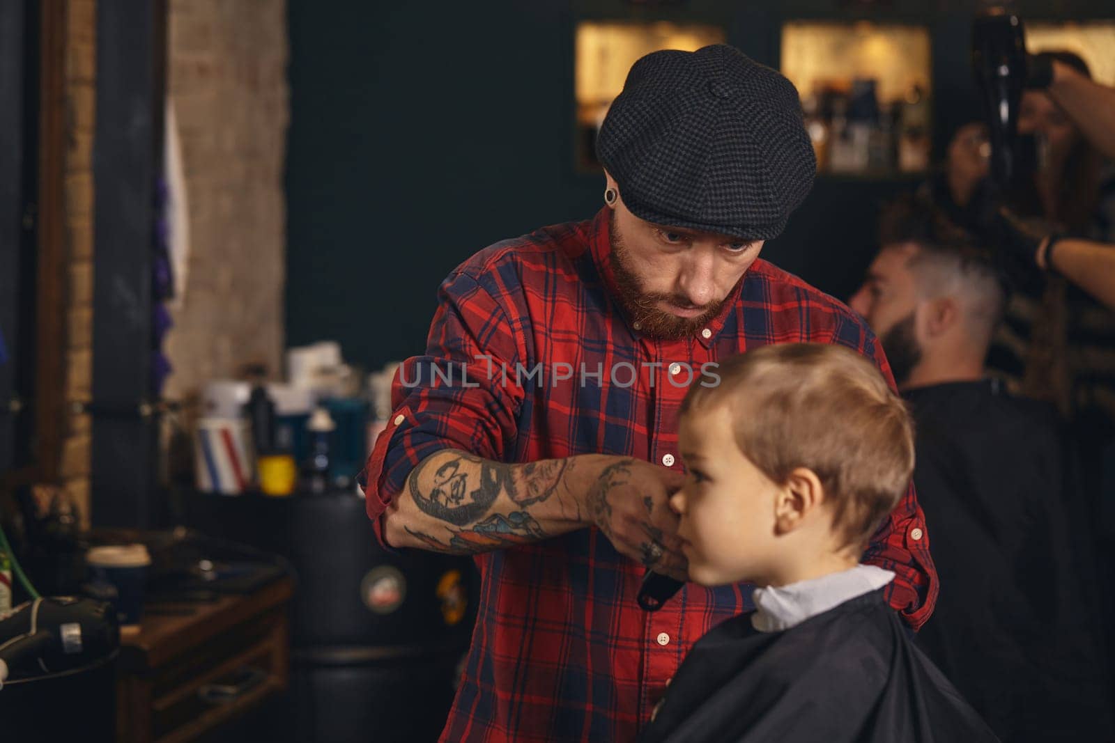 A pretty blonde boy happy to be on the haircut with a professional hairdresser. Blond little boy having a haircut at hair salon. Hairdresser's hands making hairstyle to child at barbershop