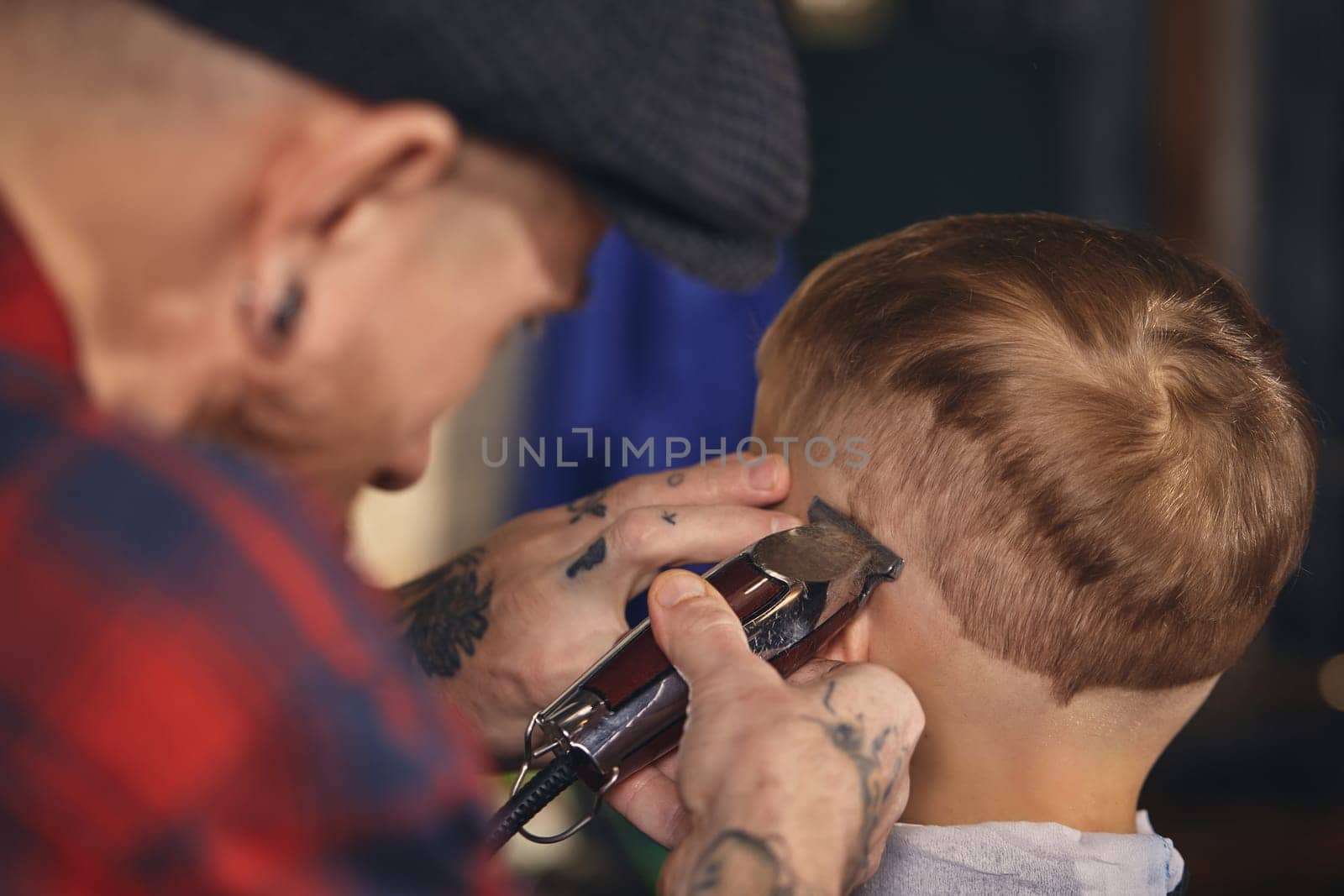 A pretty blonde boy happy to be on the haircut with a professional hairdresser. Blond little boy having a haircut at hair salon. Hairdresser's hands making hairstyle to child at barbershop