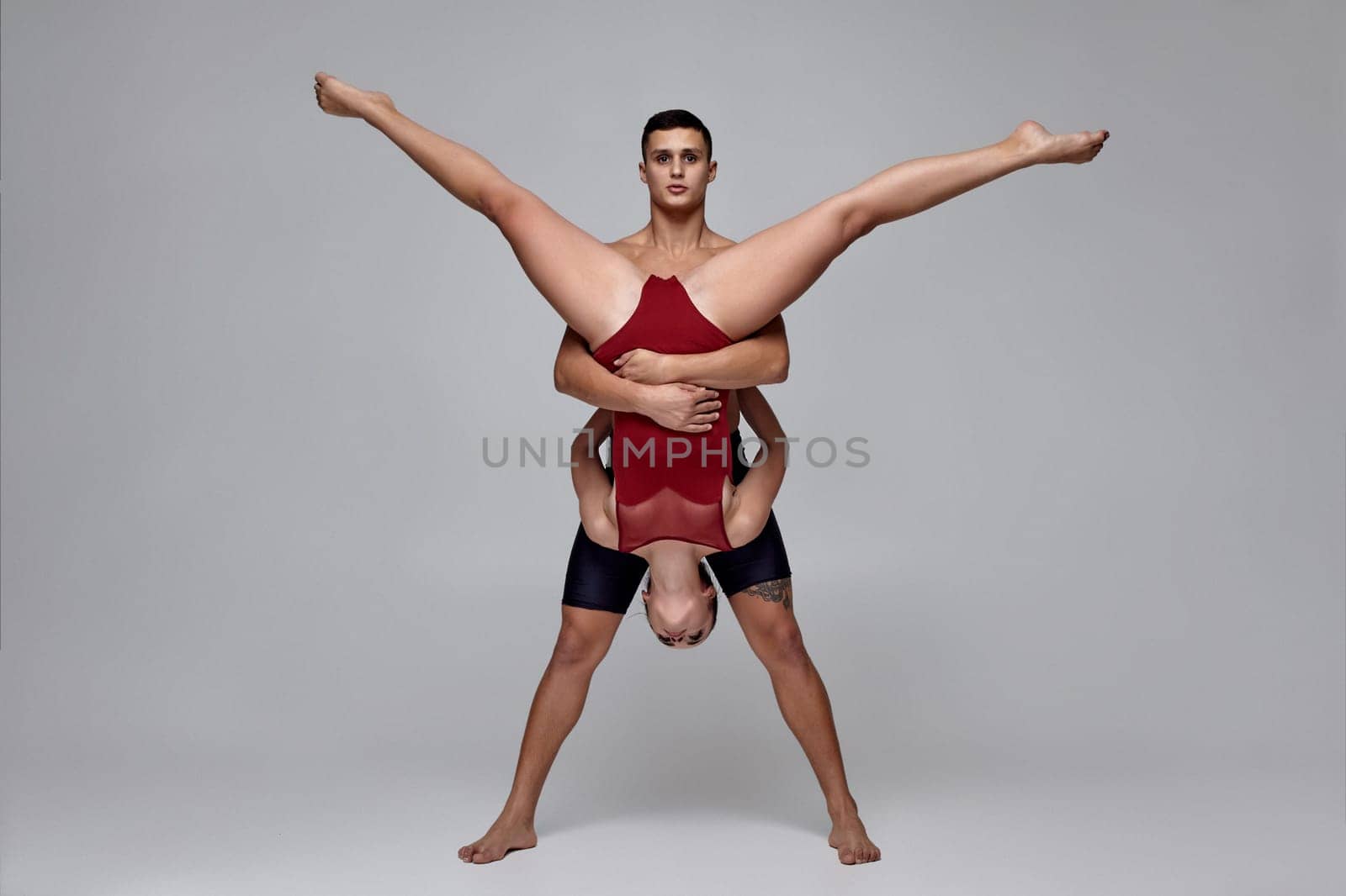 The couple of a young modern ballet dancers are posing over a gray studio background. Man in black shorts and woman in a red swimwear are dancing together. Ballet and contemporary choreography concept. Art photo.
